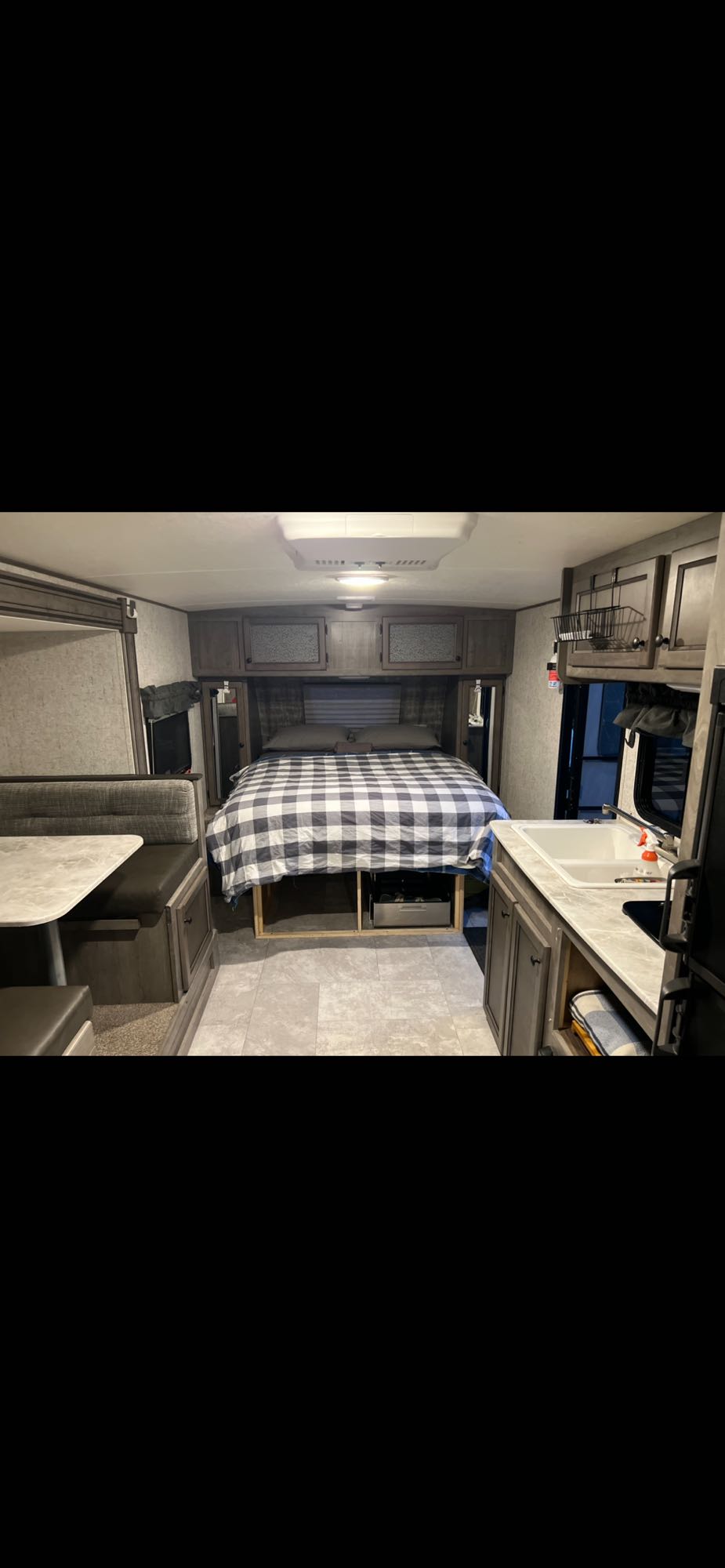 Interior of an RV rental showing a bed with plaid comforter, dinette, and small kitchen setup.. Coachmen Apex Nano 2019