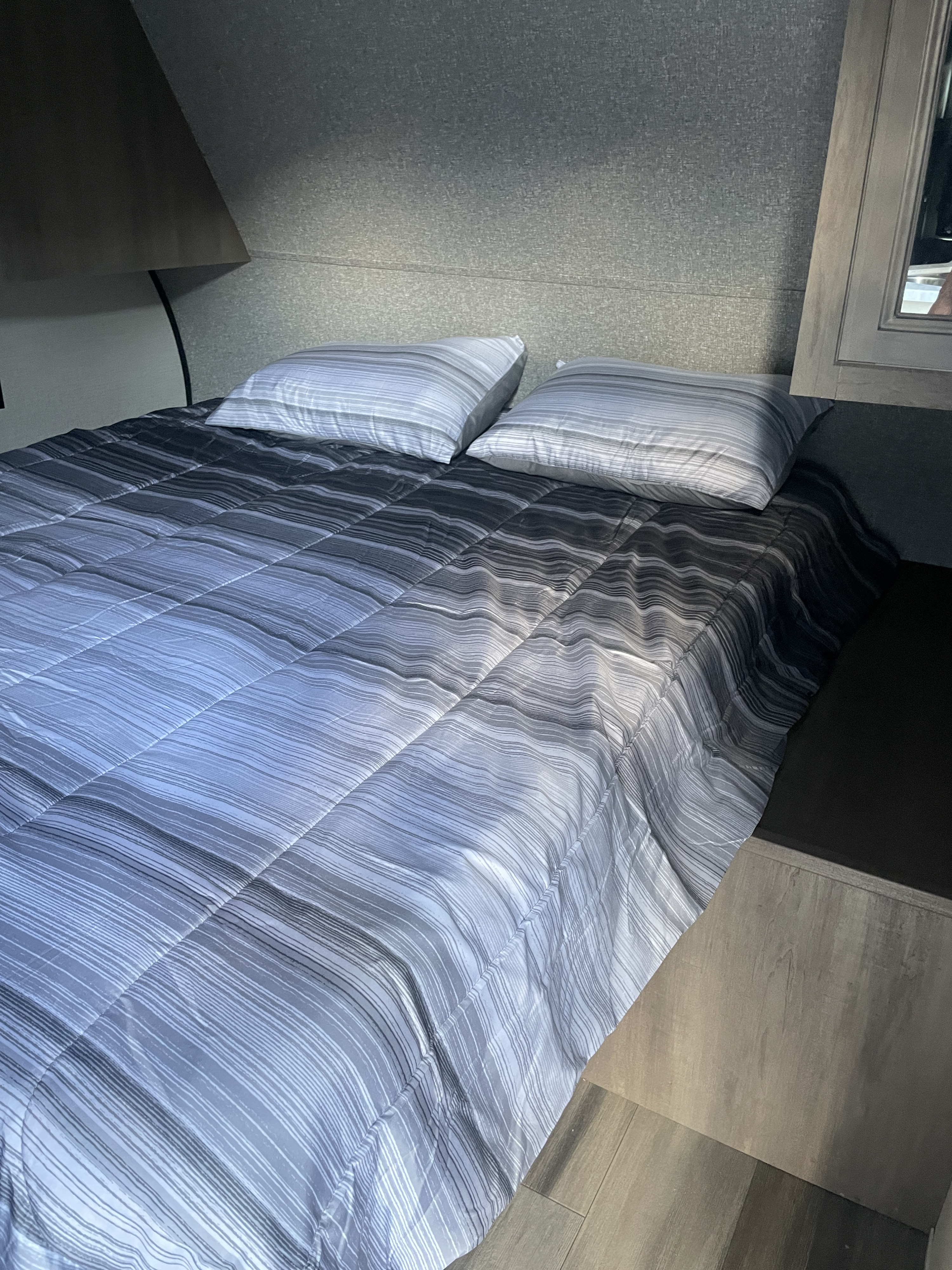 Close-up of a neatly made bed in an RV rental bedroom, featuring a grey and white striped comforter and two pillows.. Highland Ridge RV Open Range 2022