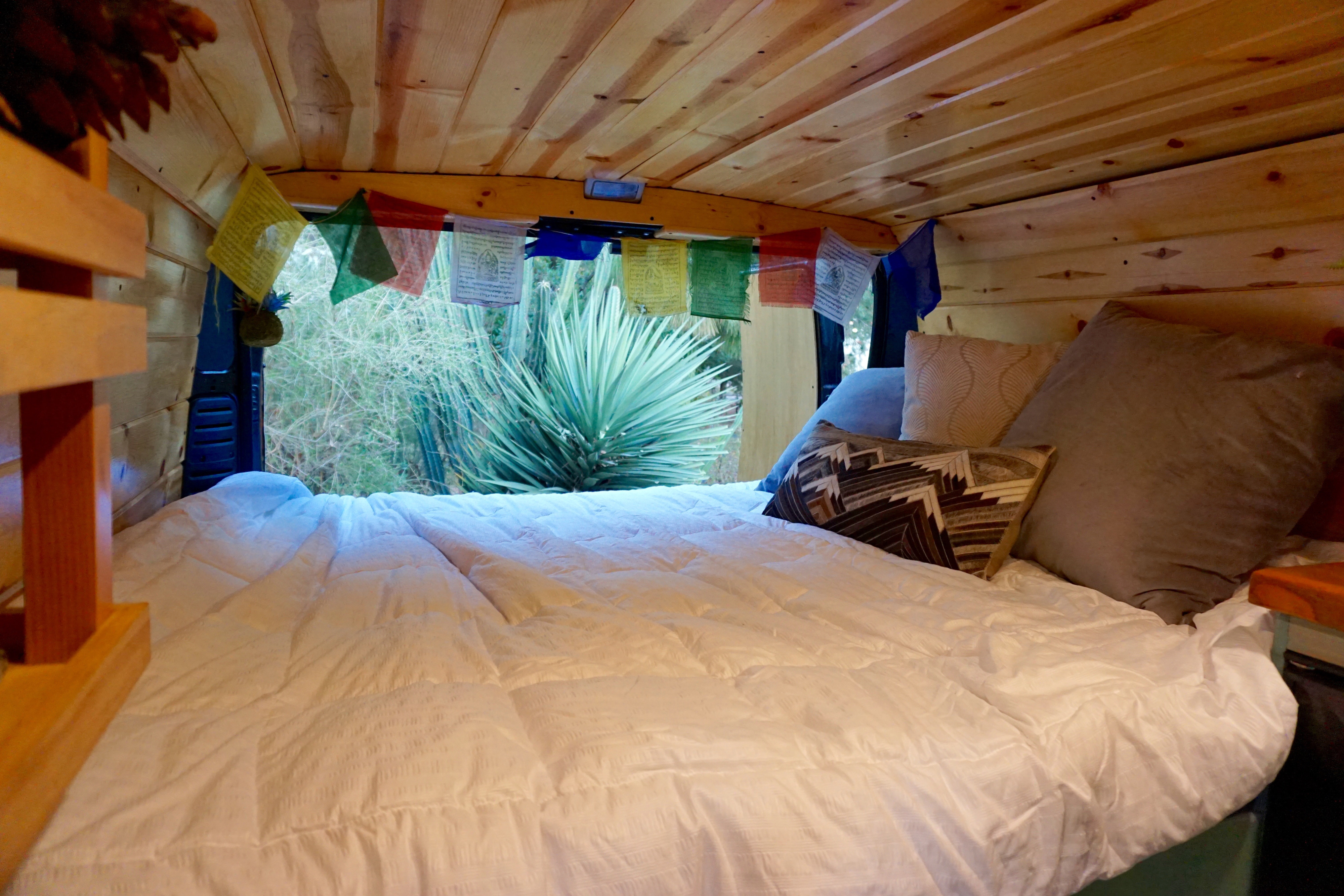 Experience comfort in this RV rental's cozy bed. Wood-paneled interior, prayer flags, and a desert view awaits.. Dodge Sprinter Van 2018