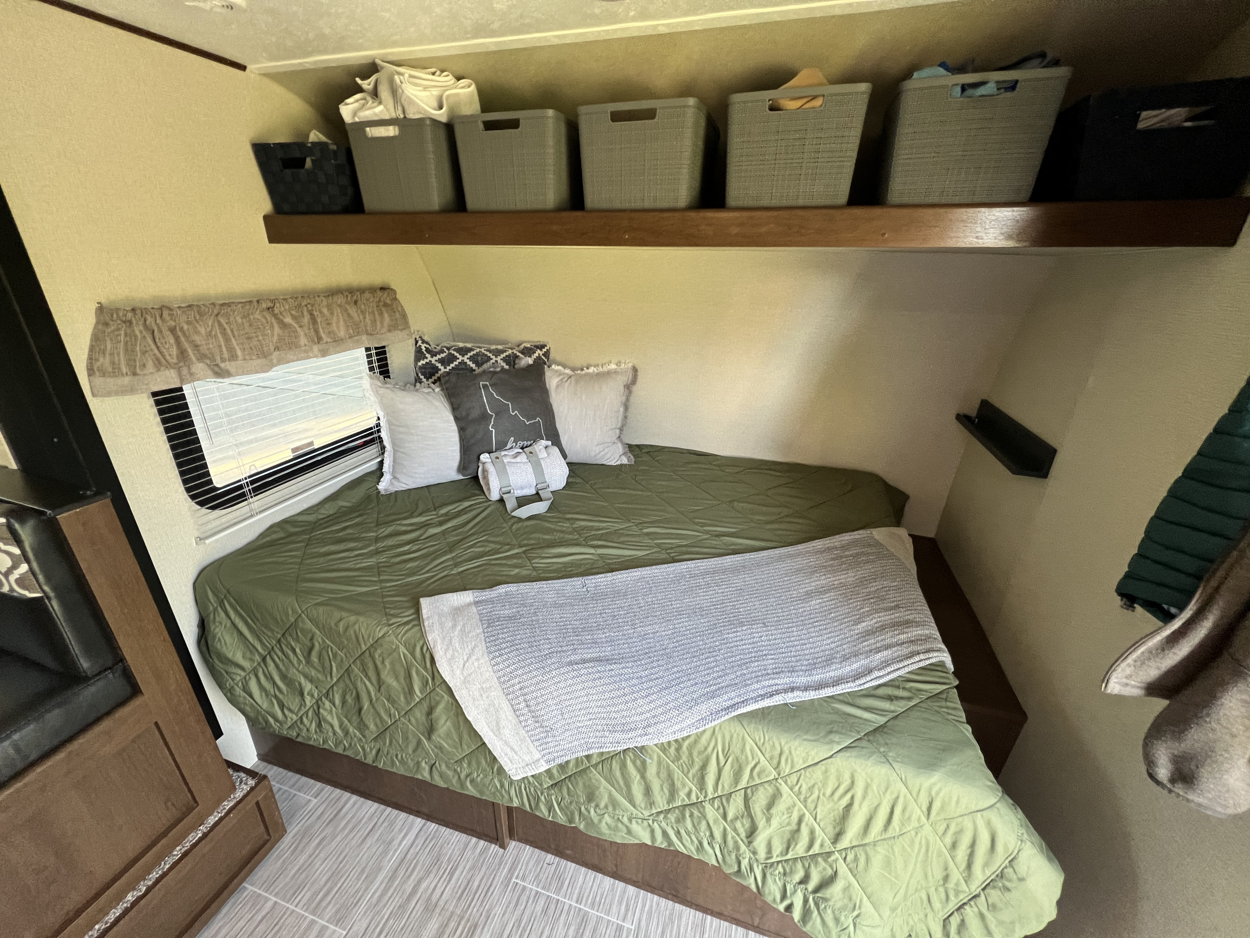 Cozy RV rental bedroom: A neatly made bed with green comforter, pillows, and overhead storage bins for organized travel.. Navi Navi Trailer 2019