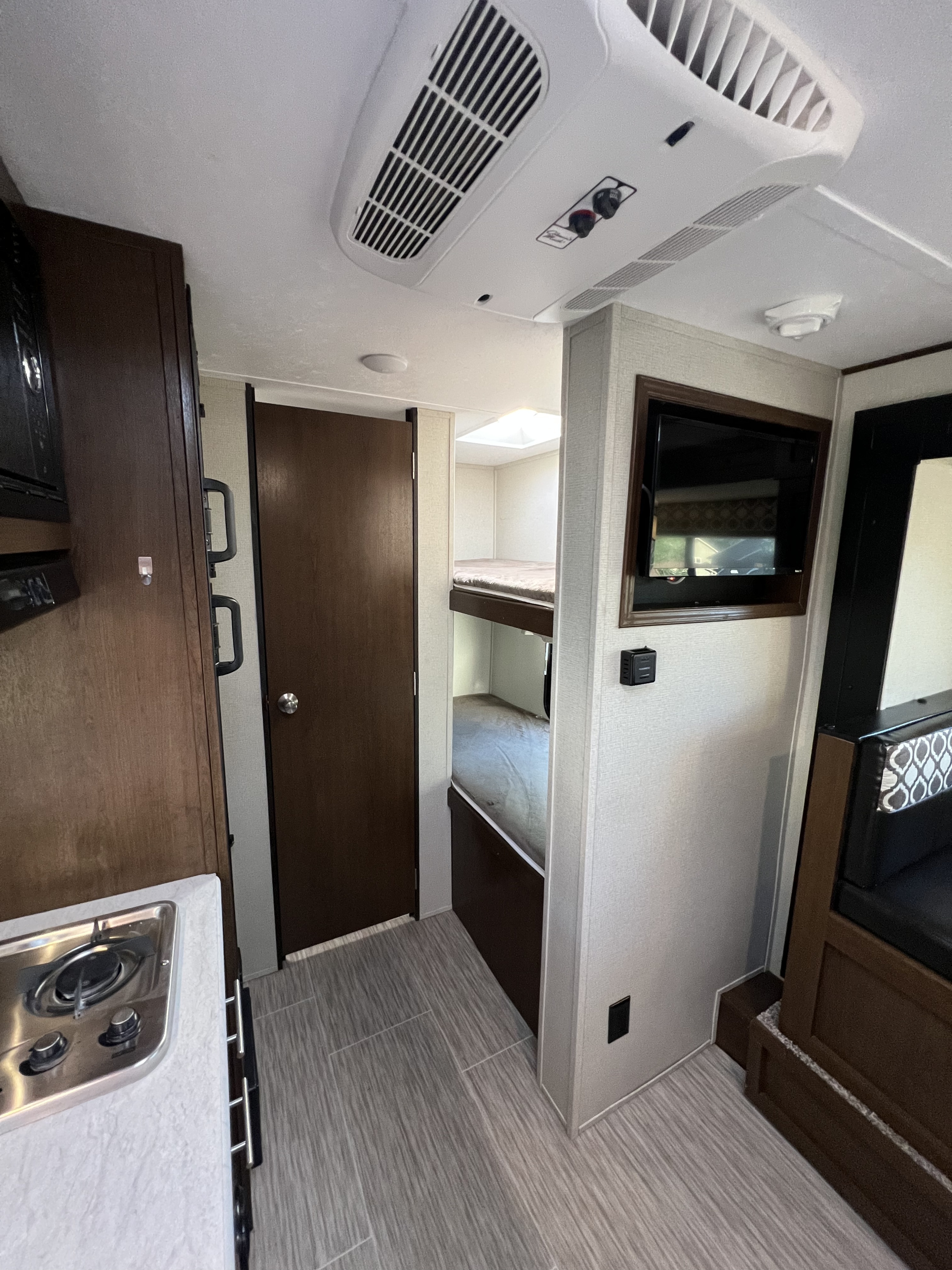 This RV rental interior features a compact kitchen, bunk beds, and a cozy living area with a TV, ideal for travel.. Navi Navi Trailer 2019
