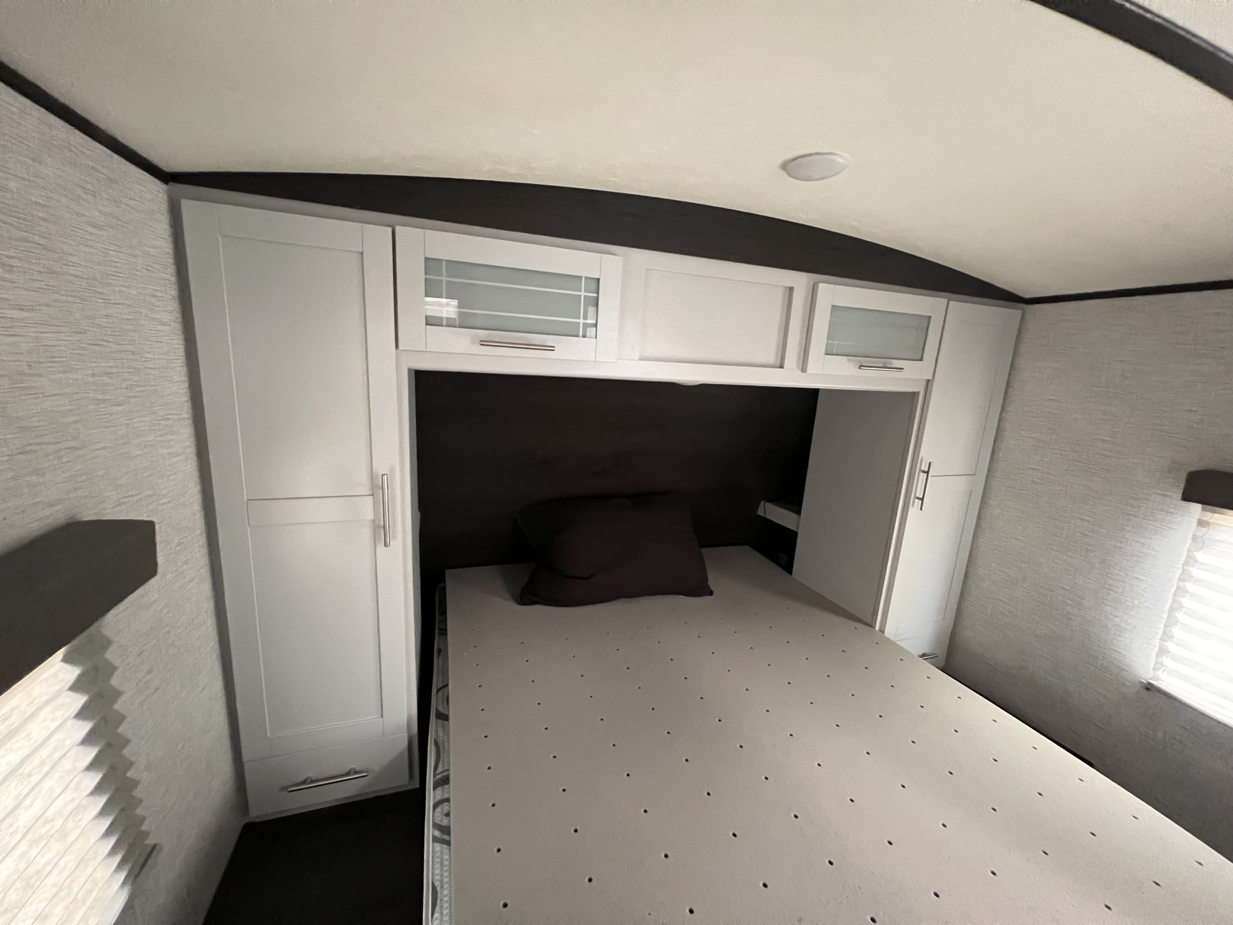 RV rental bedroom: cozy space with white cabinets, textured walls, and a comfortable bed with a topper.. Keystone Bullet 2021