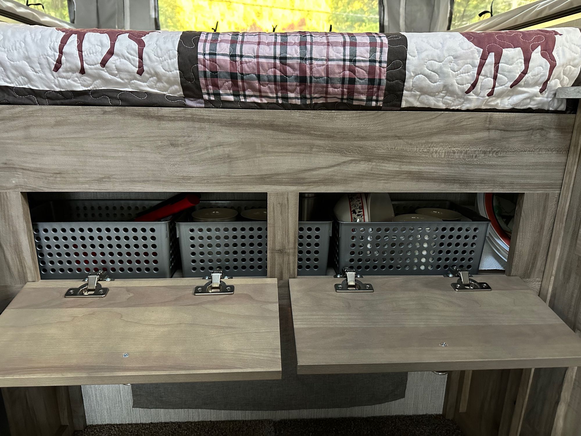 Under-bed storage in an RV rental, featuring organized baskets for kitchenware and a deer-themed quilt.. Forest River Travel lite 2022