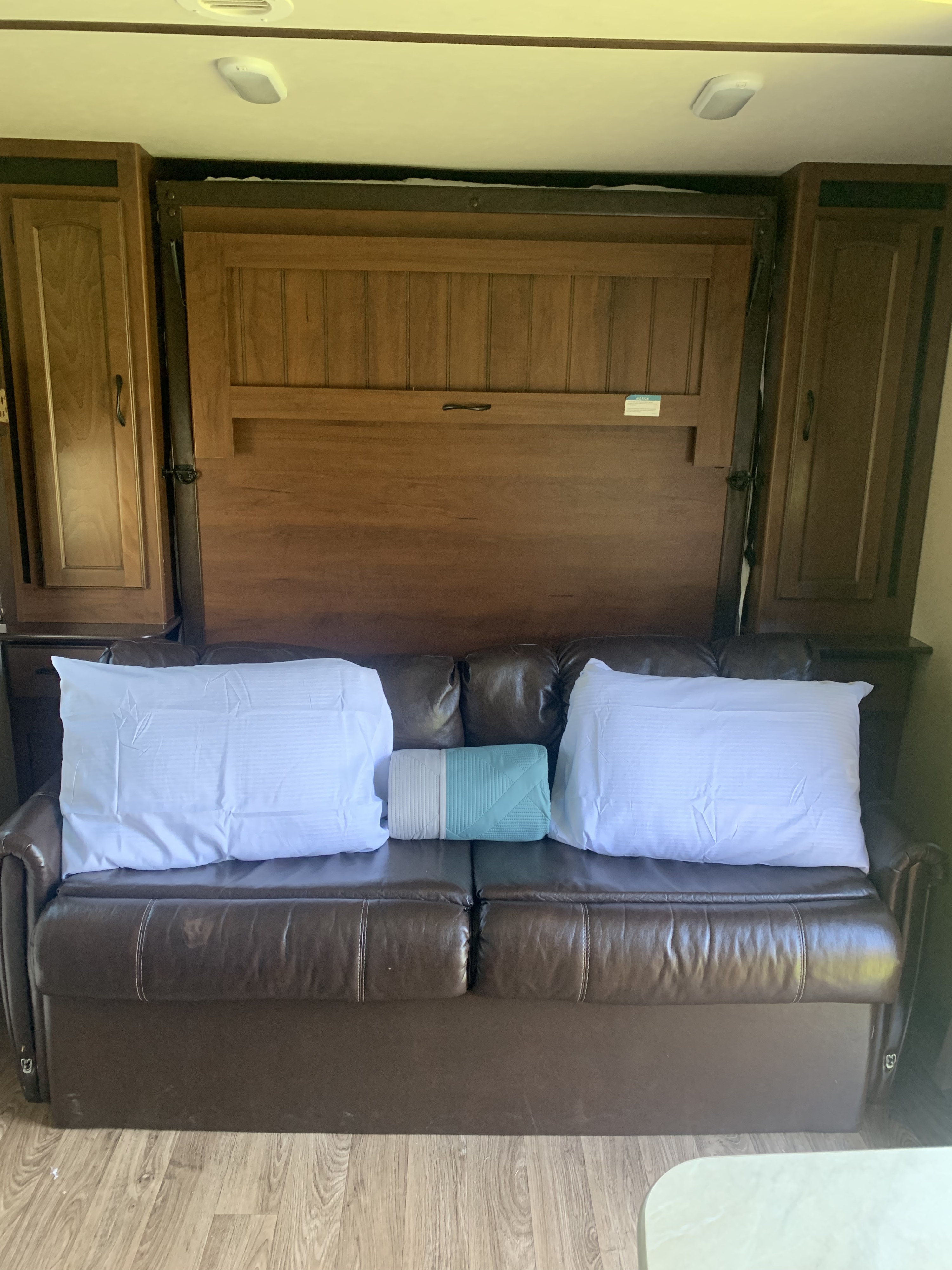 RV rental interior featuring a brown sofa, pillows, and a clever wall-mounted Murphy bed system with wooden cabinets.. Jayco White Hawk Ultra Lite 2015