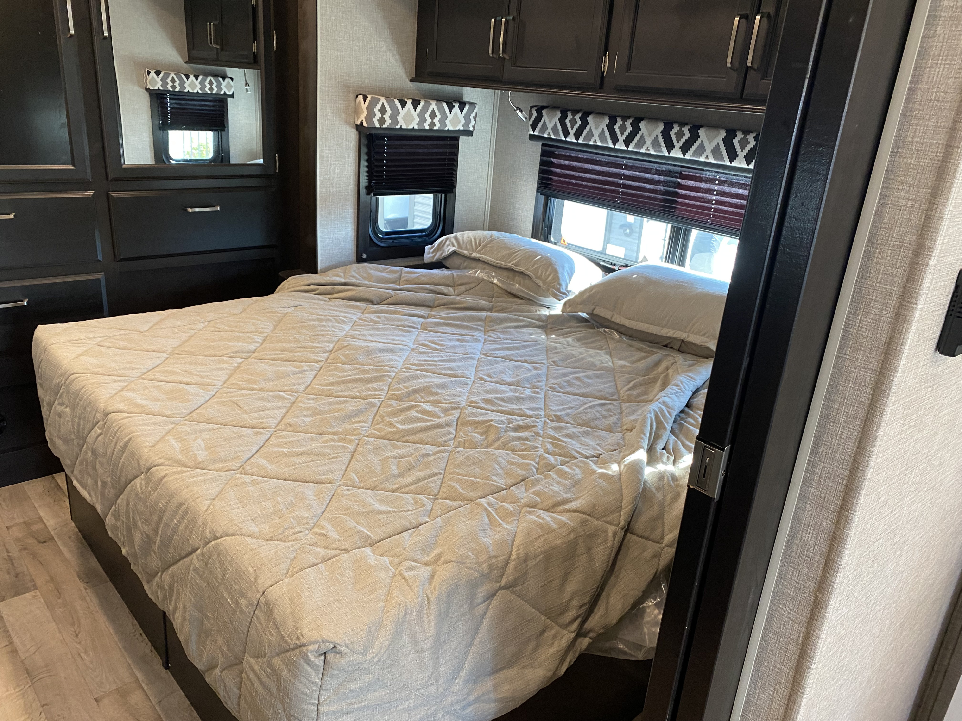 RV rental bedroom: a comfortable quilted bed, dark wood cabinets, and windows with patterned valances.. Entegra Coach Odyssey 2022