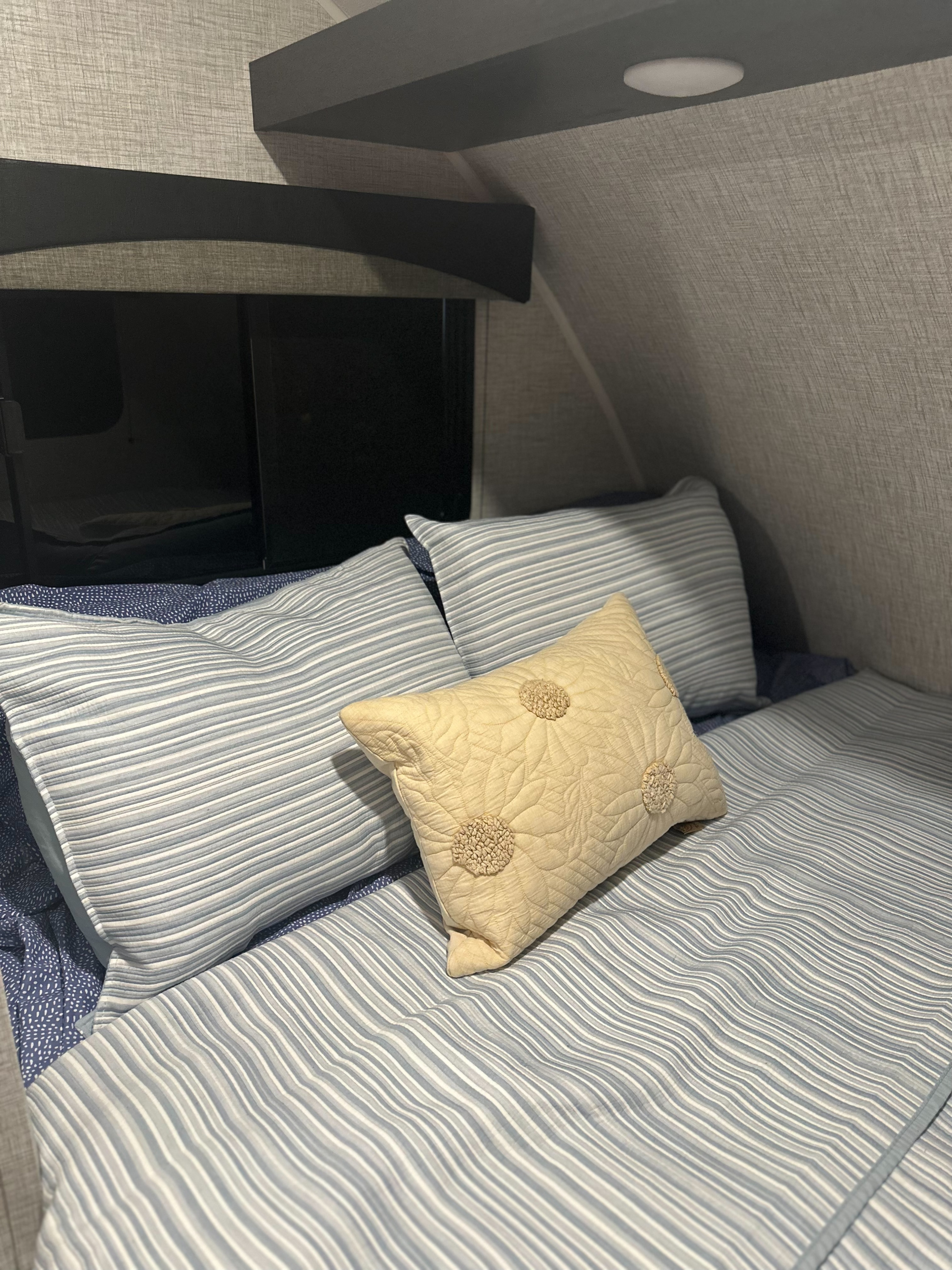 A cozy RV bed featuring blue and white striped bedding and a decorative pillow, ready for your next rv rental adventure.. Braxton Creek Bushwhacker Plus 2021