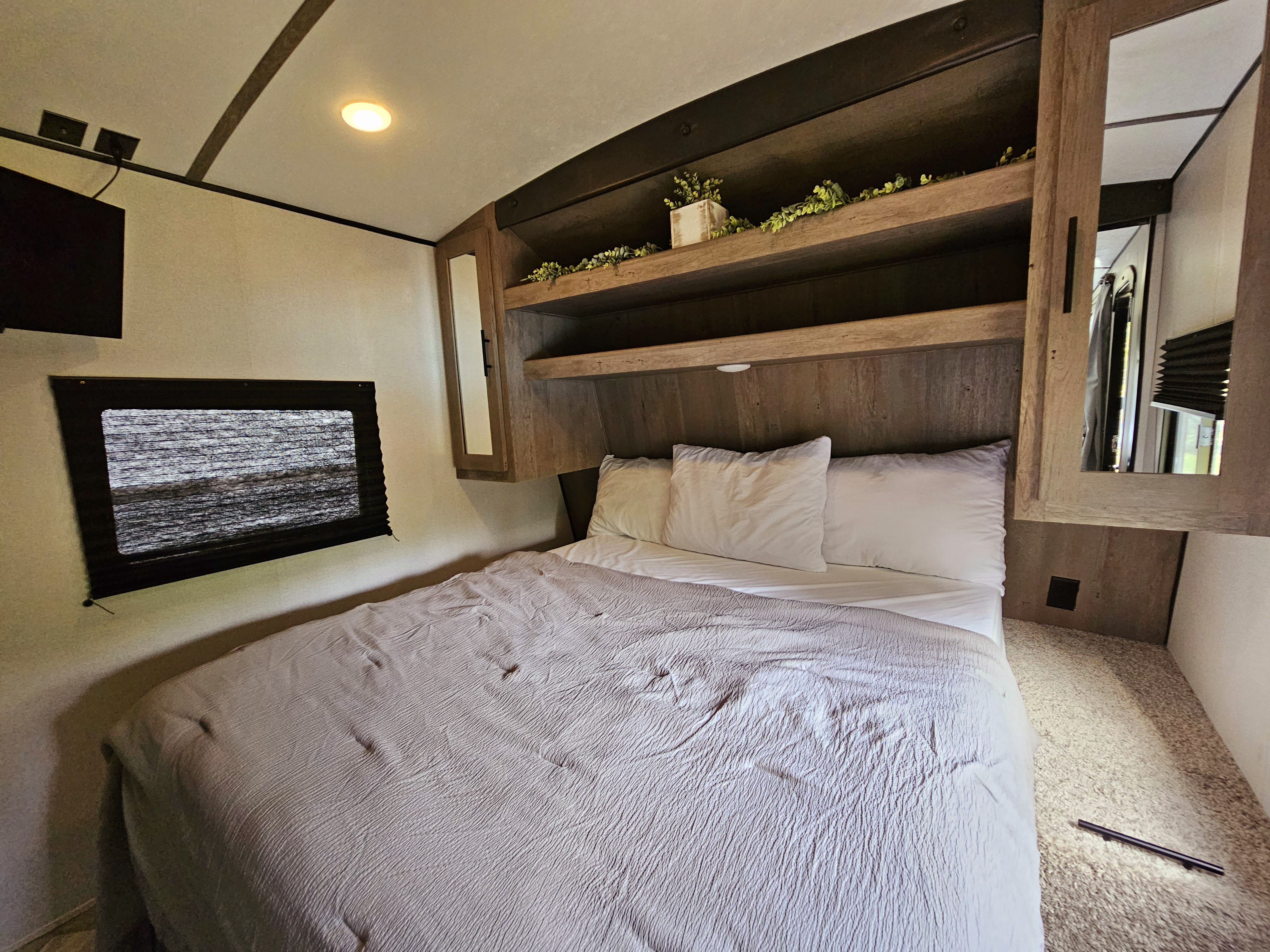 Cozy RV rental bedroom featuring a queen bed, wall-mounted TV, built-in shelving, and a mirrored wardrobe.. Keystone Springdale 2023