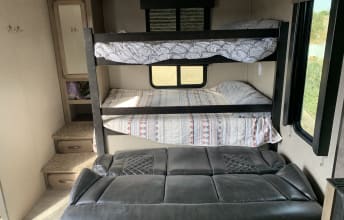 Inside an RV rental: a cozy bunk bed sleeping area over a comfortable sofa, plus built-in storage. Ideal for family trips.. Grand Design Transcend Xplor 2020