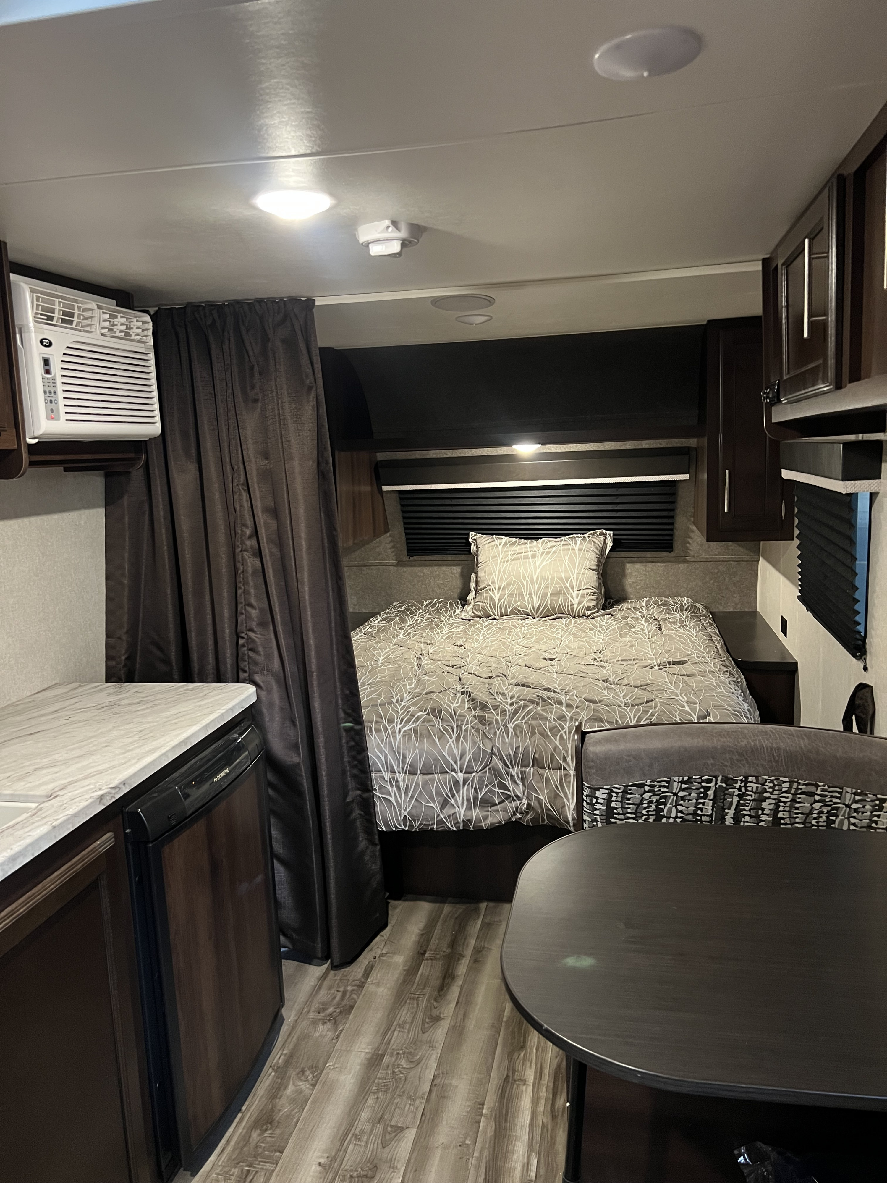 Inside a modern RV rental: bedroom with patterned bedding, compact kitchen with mini-fridge, and dining area.. Jayco Jay Flight SLX 2020