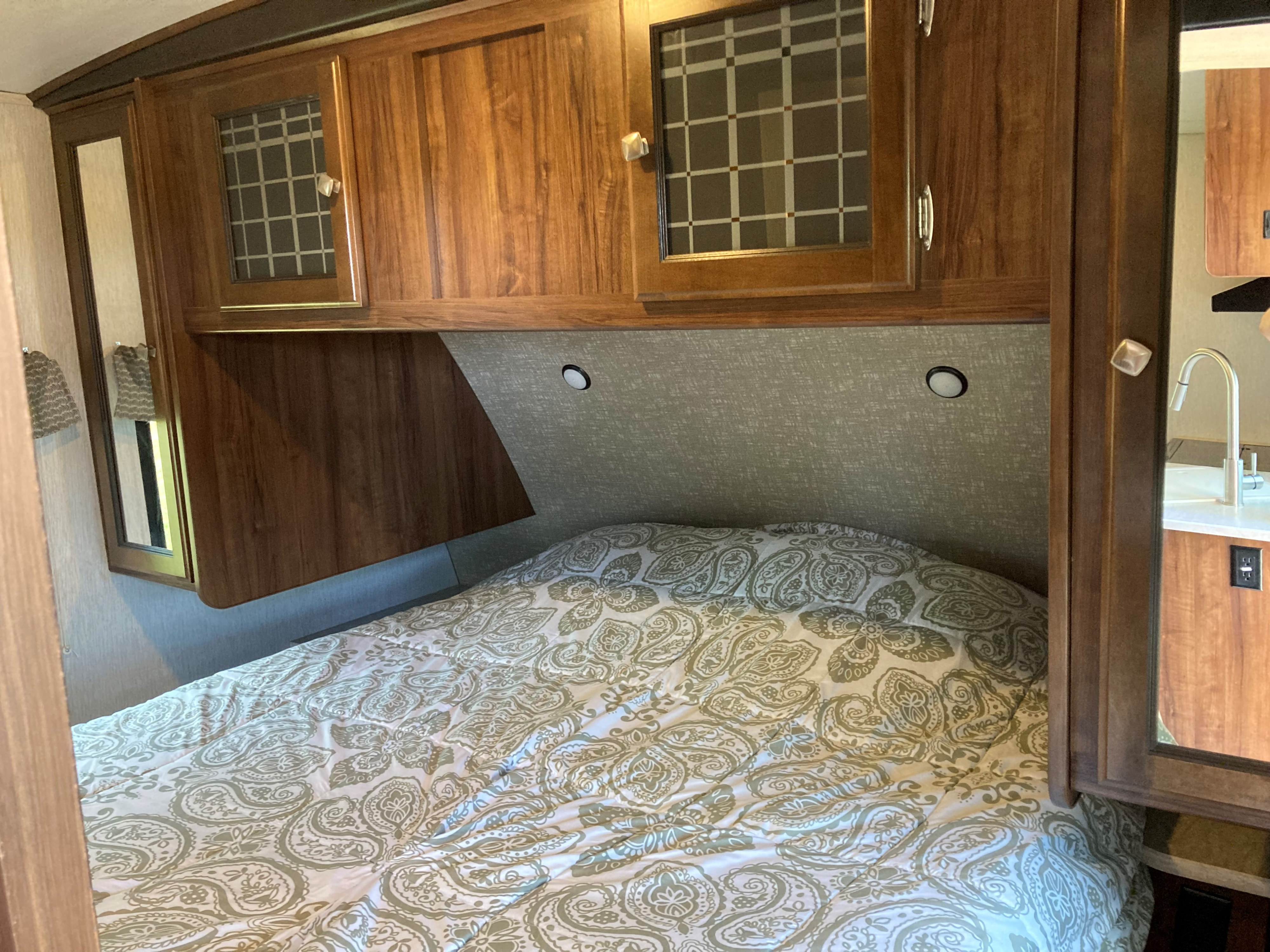 Interior of an RV rental bedroom featuring a paisley comforter, compact wooden cabinets, and bedside lights.. Heartland RVs Mallard 2018