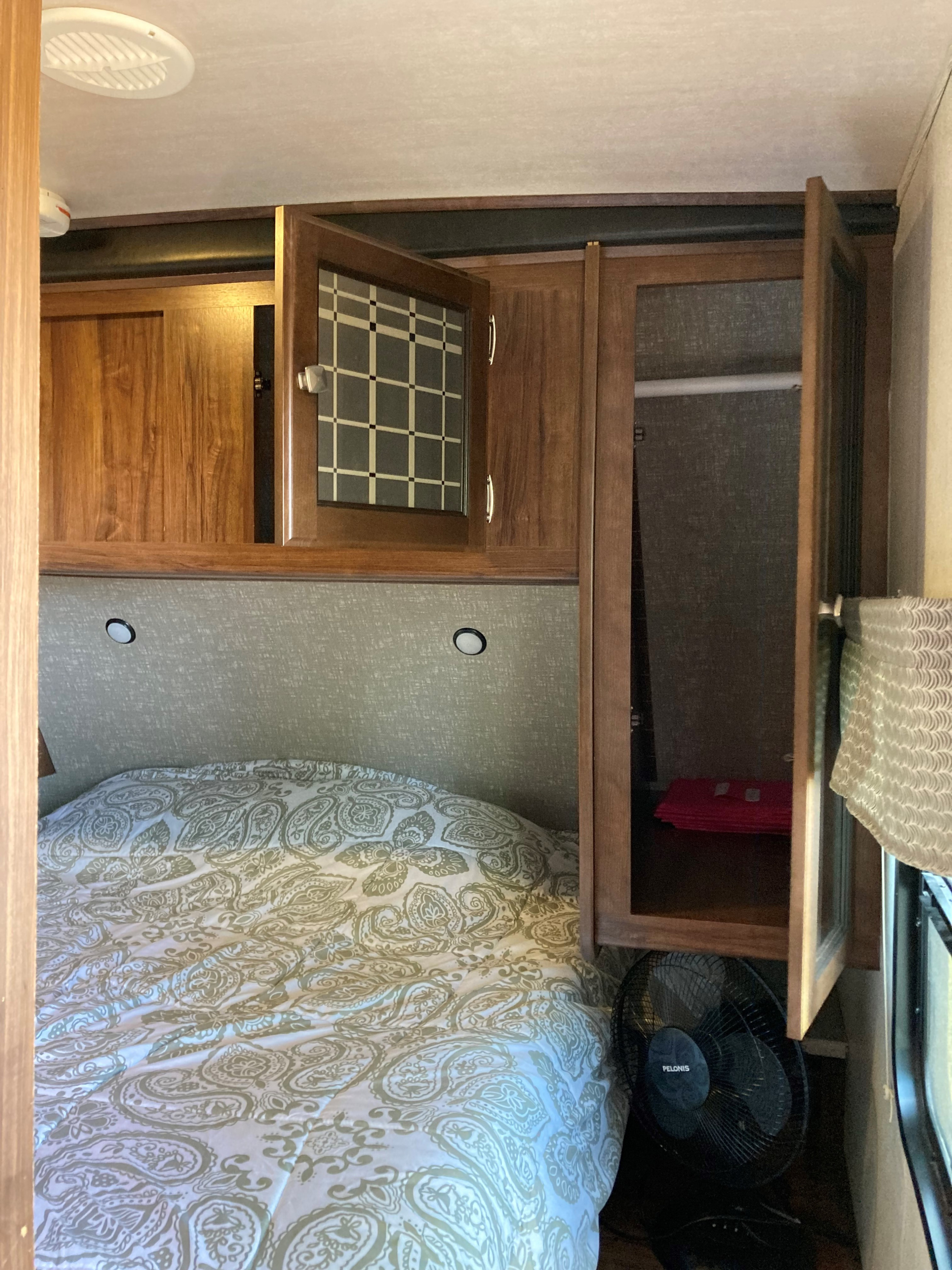 RV rental bedroom: cozy bed, overhead wooden cabinets (some open), and a fan, offering comfortable storage.. Heartland RVs Mallard 2018
