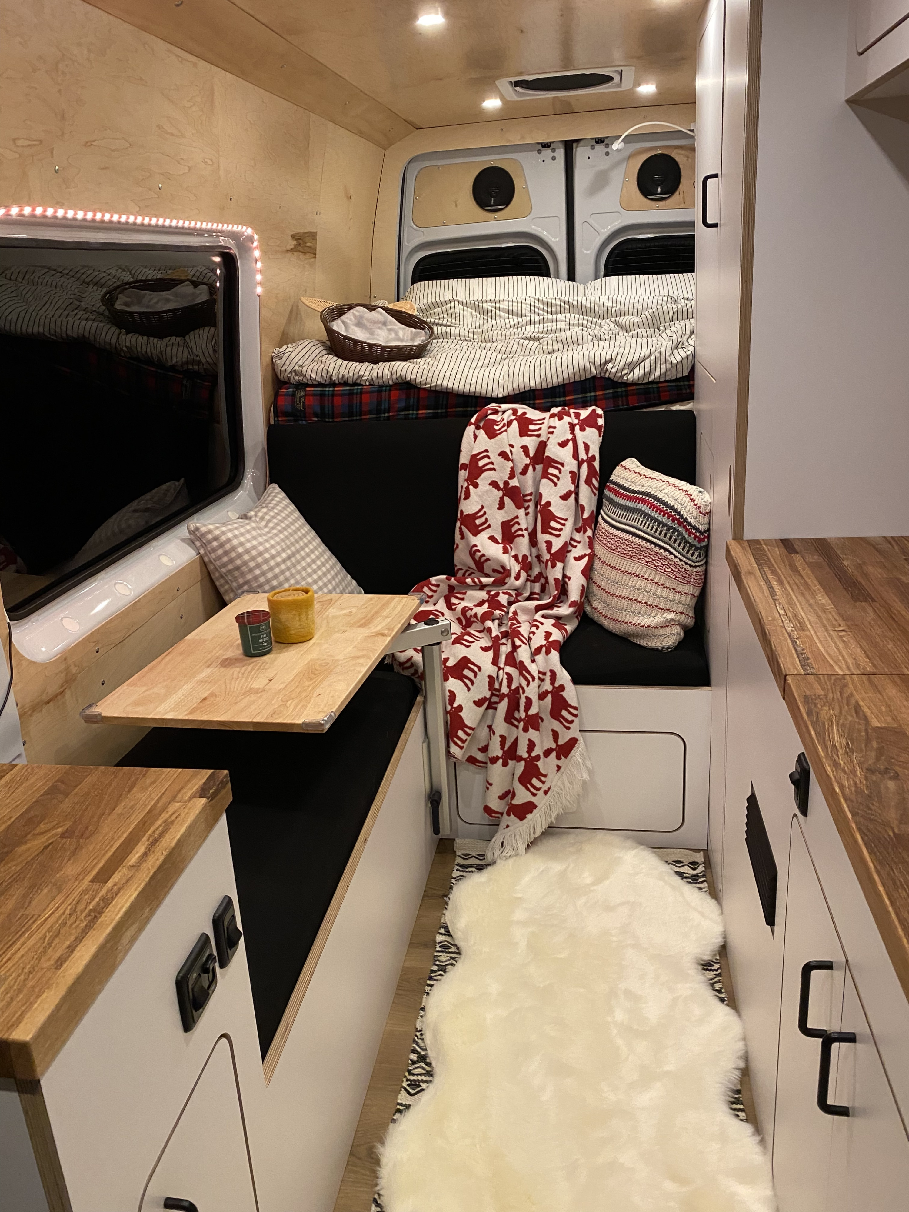 Cozy RV rental interior with a comfortable bed, bench seating, and wooden finishes, perfect for compact living.. VanCraft VanCraft Class B 2021
