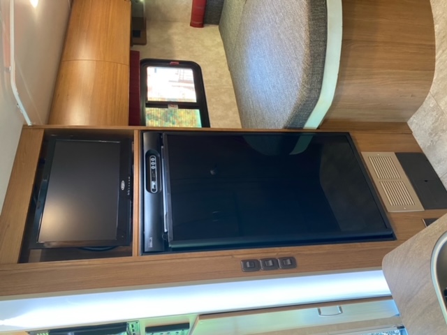 rv rental: View of an RV interior featuring a modern entertainment center with dual TVs, rich wood cabinetry, and a plush, curved bed.. Winnebago Trend 2015