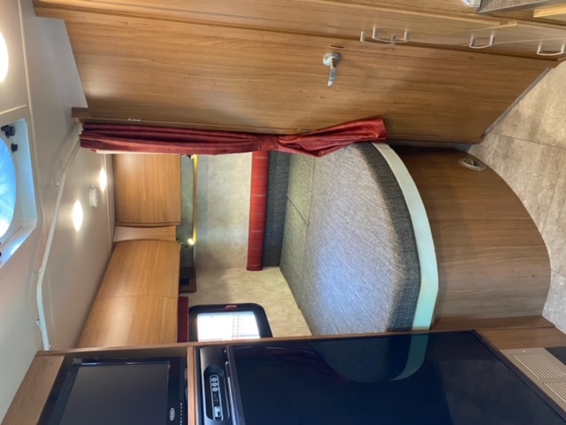 Interior of an RV rental: curved bed with gray cushions, rich wooden cabinetry, and media center. Compact, well-lit living space.. Winnebago Trend 2015