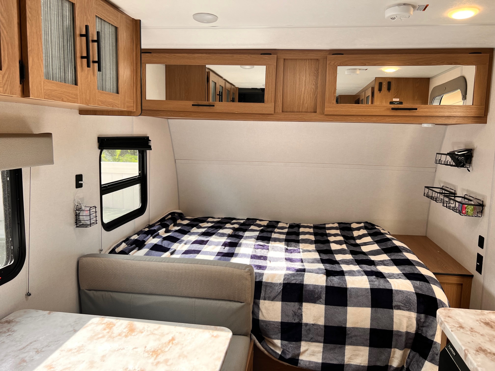Inside a modern RV rental: a compact bedroom with plaid bedding, overhead cabinets, and dinette.. Avenger LT 2022