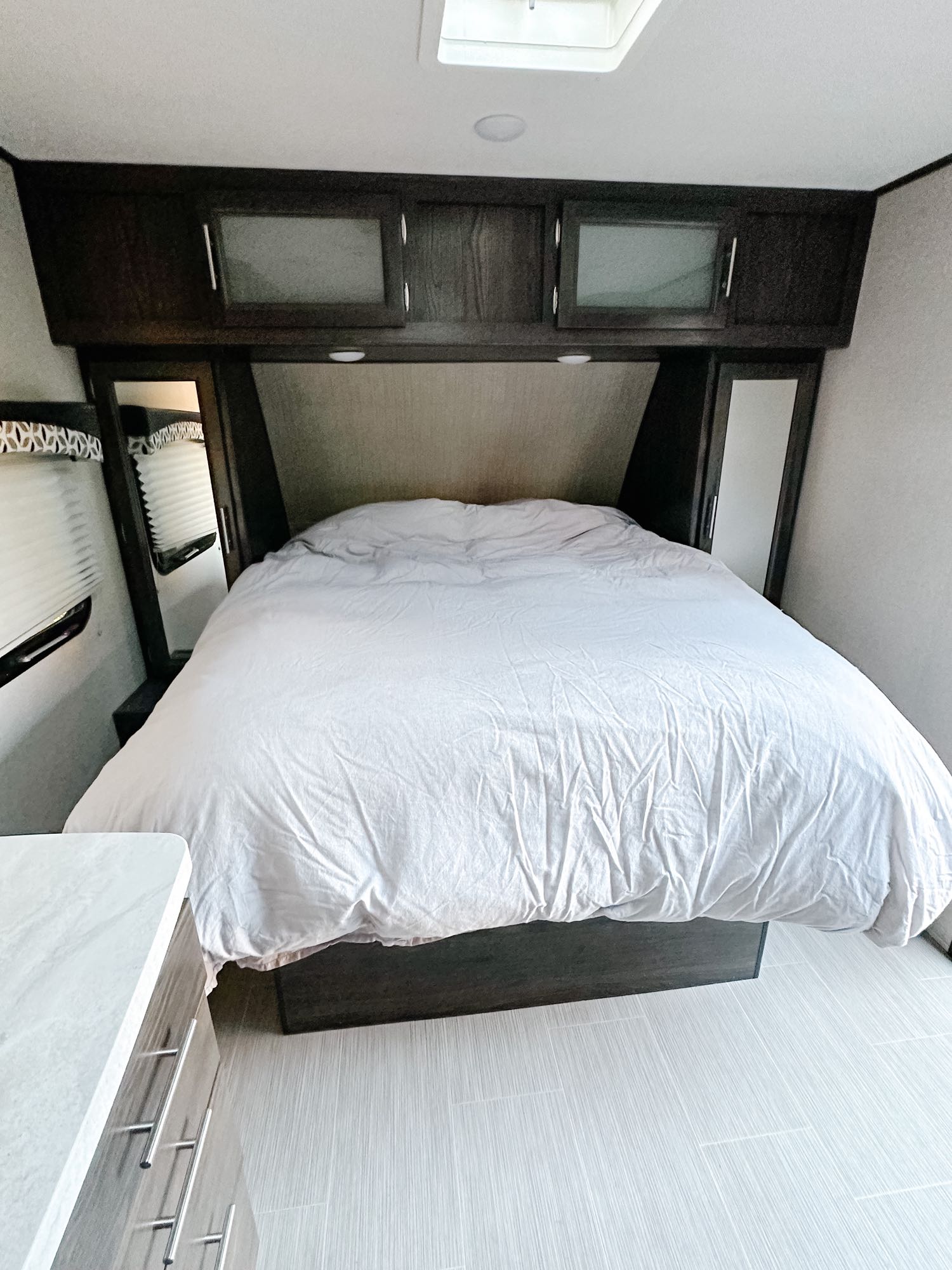 Inside an RV rental bedroom: a large bed with white bedding, dark overhead cabinets, and light flooring provide a modern, clean space.. Dutchmen Kodiak Ultimate 2018