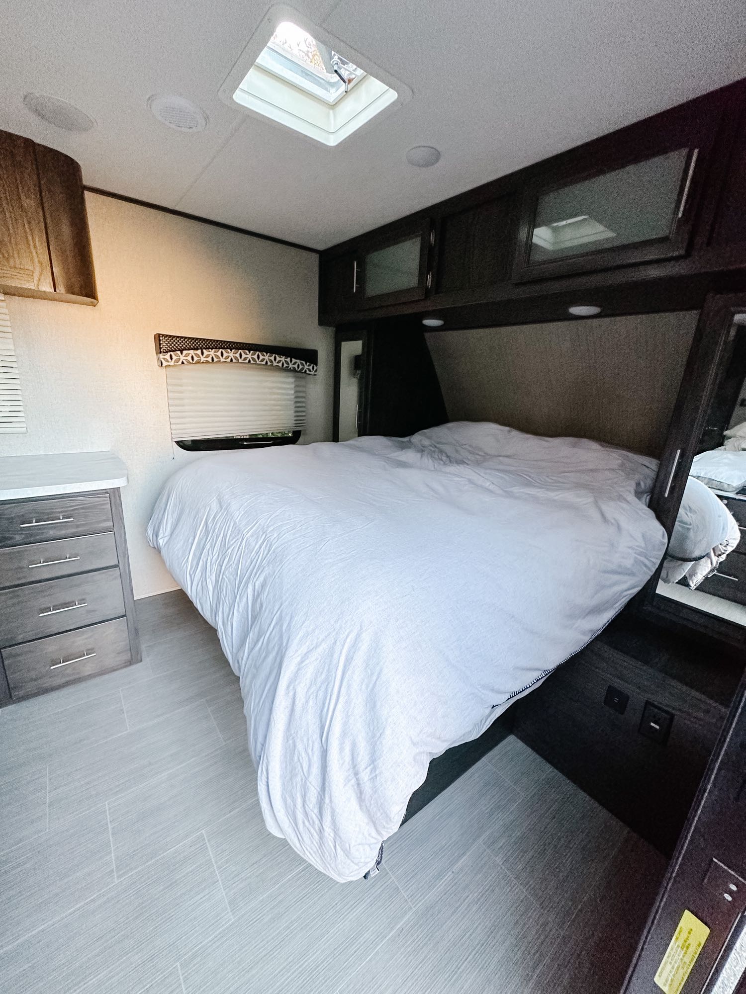 Inside a modern RV rental: a comfortable bedroom with a large bed, overhead storage, and dresser, bathed in light from the skylight.. Dutchmen Kodiak Ultimate 2018