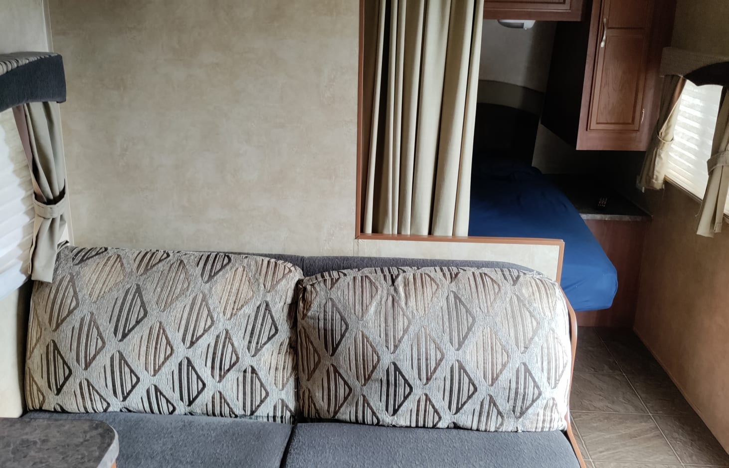 RV rental interior: A cozy living area with a sofa, patterned pillows, and a private bunk bed with blue bedding.. Jayco Jay Flight 2010