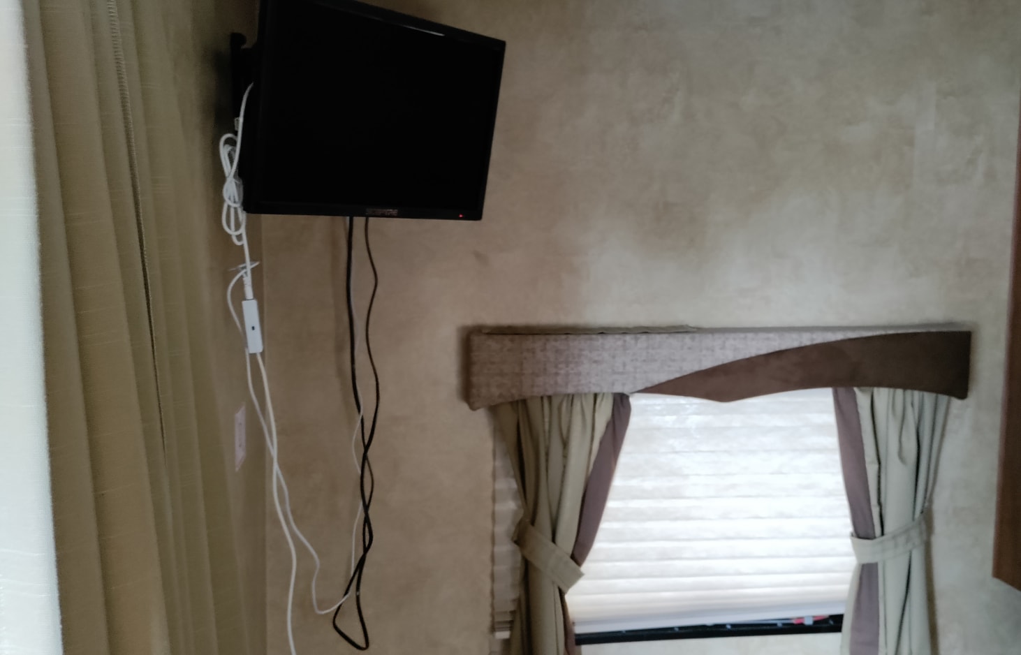 RV rental interior: Wall-mounted TV with trailing cables above a window with decorative valance & curtains.. Jayco Jay Flight 2010