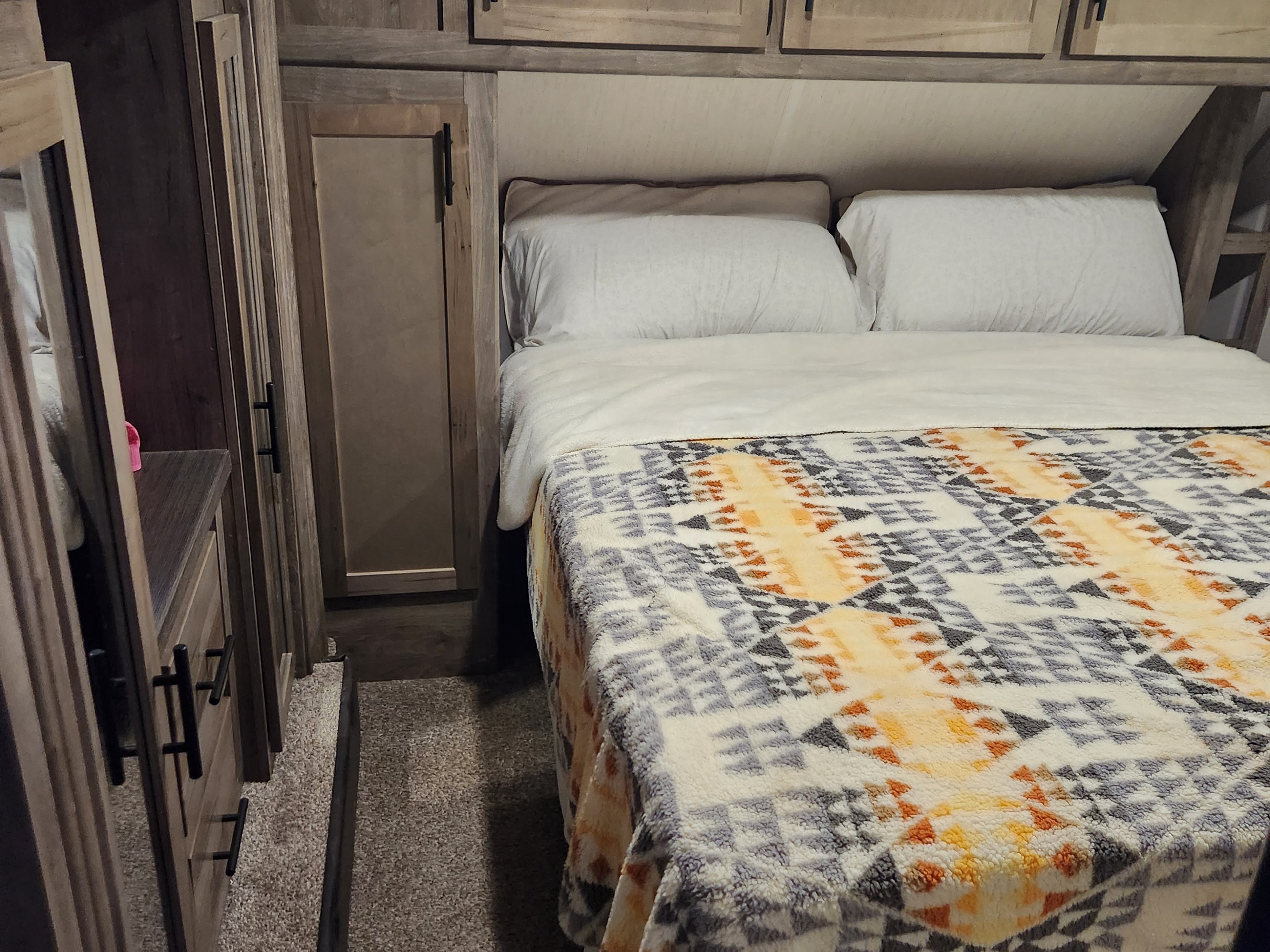 RV rental bedroom featuring a cozy bed with a patterned blanket, overhead cabinets, and built-in dresser.. Forest River Cherokee Wolf Pack Toy Hauler 2021