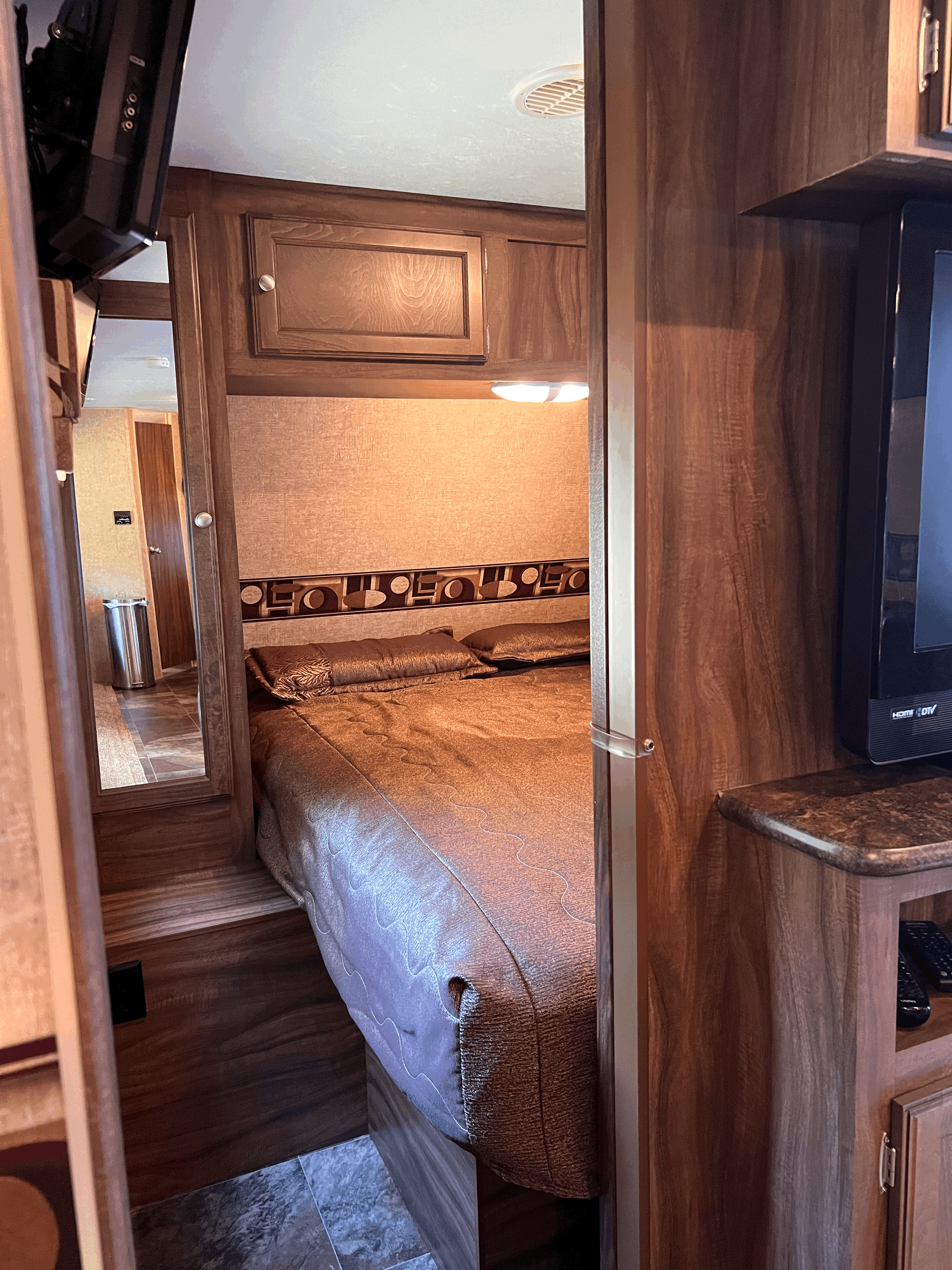 Inside an RV rental: a cozy bedroom with a large bed, wood cabinetry, TV, and mirrored hallway.. Sportsmen Show Stopper 2015