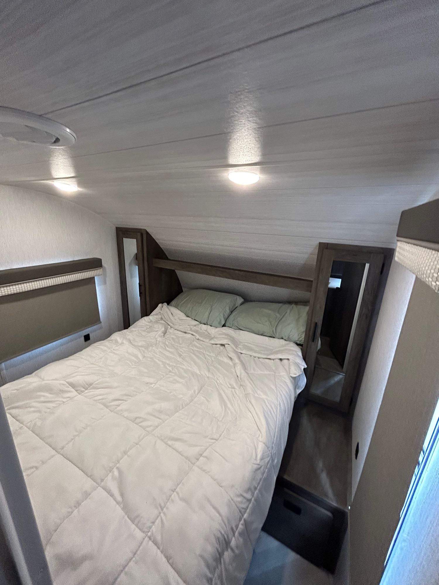 Inside a modern RV rental bedroom, featuring a large bed with a white comforter, pillows, and integrated storage.. Forest River Wildwood X-Lite 2022