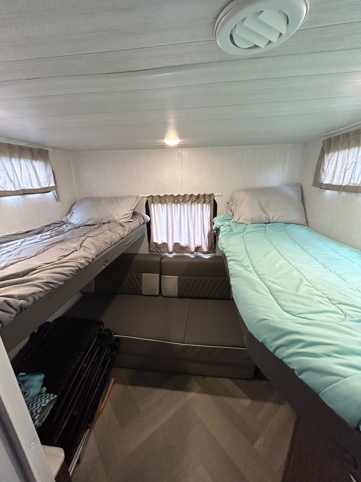 An RV rental bunkhouse with two made beds, a convertible seating area below, and wood-look flooring.. Forest River Wildwood X-Lite 2022