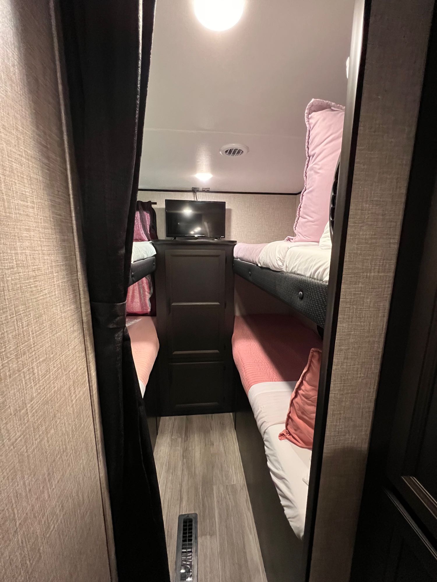 Cozy RV rental bunk beds with pink & white bedding, a TV, and privacy curtain, offering a comfy sleeping area.. Jayco Jay Flight 2023