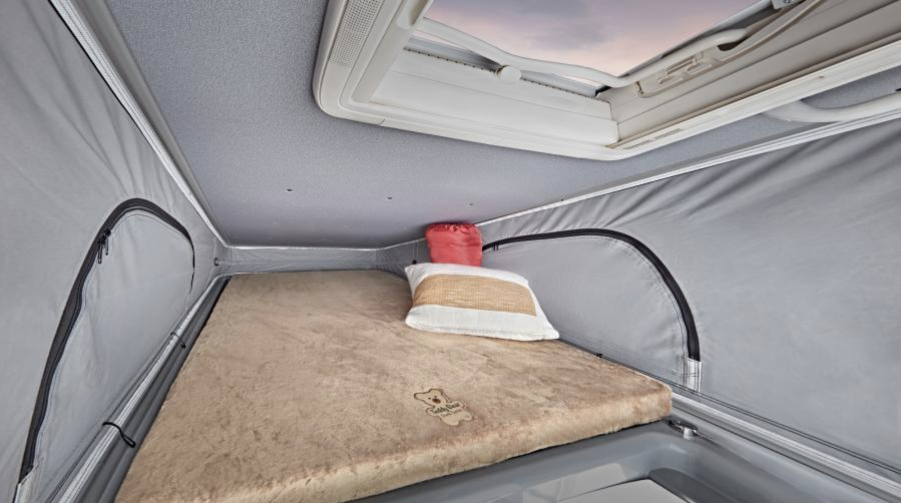 Cozy pop-top sleeping area in an RV rental. Features a fluffy bed, pillow, and skylight for travel comfort.. Entegra Coach Ethos 2023