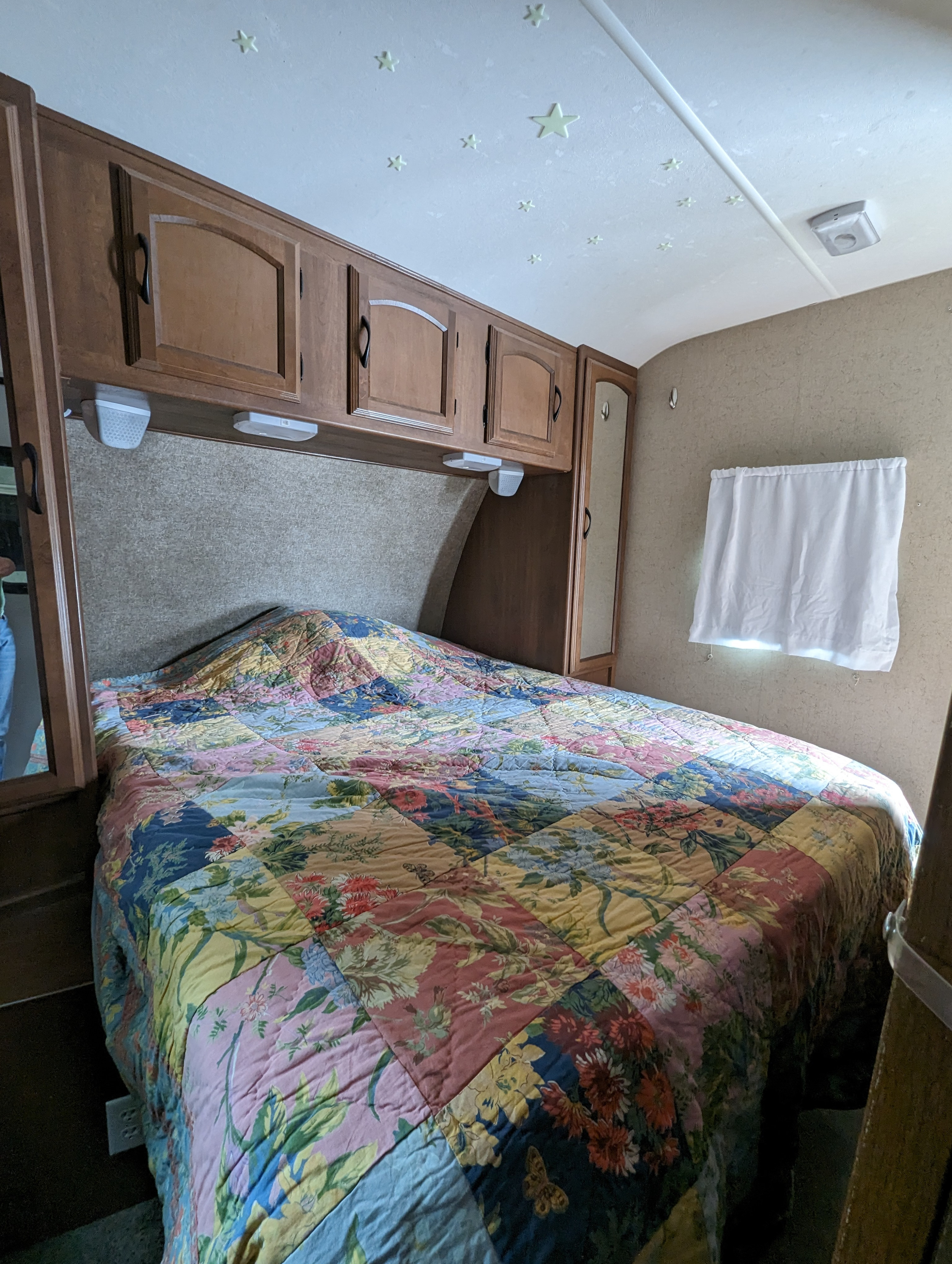 The bedroom of an RV rental features a bed with a vibrant patchwork quilt, wooden cabinets, and glowing ceiling stars.. Coachmen Freedom Express 2015
