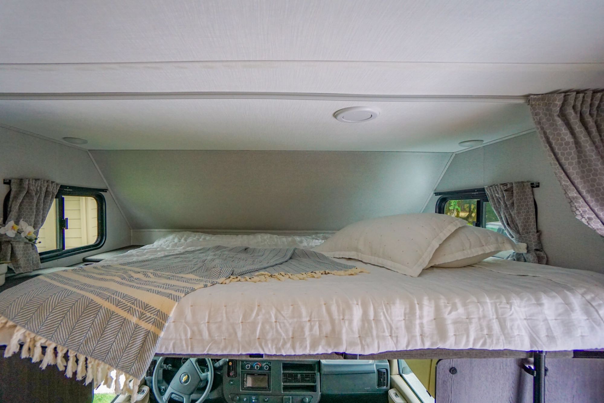 RV rental's spacious cab-over bed, dressed in white bedding & a patterned throw, ready for a cozy sleep.. Forest River Sunseeker LE 2020