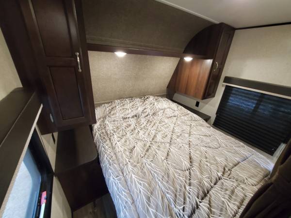 Inside a comfy RV rental bedroom: bed with leafy comforter, dark wood cabinets, and window blinds for privacy.. Jayco Jay Flight 2017