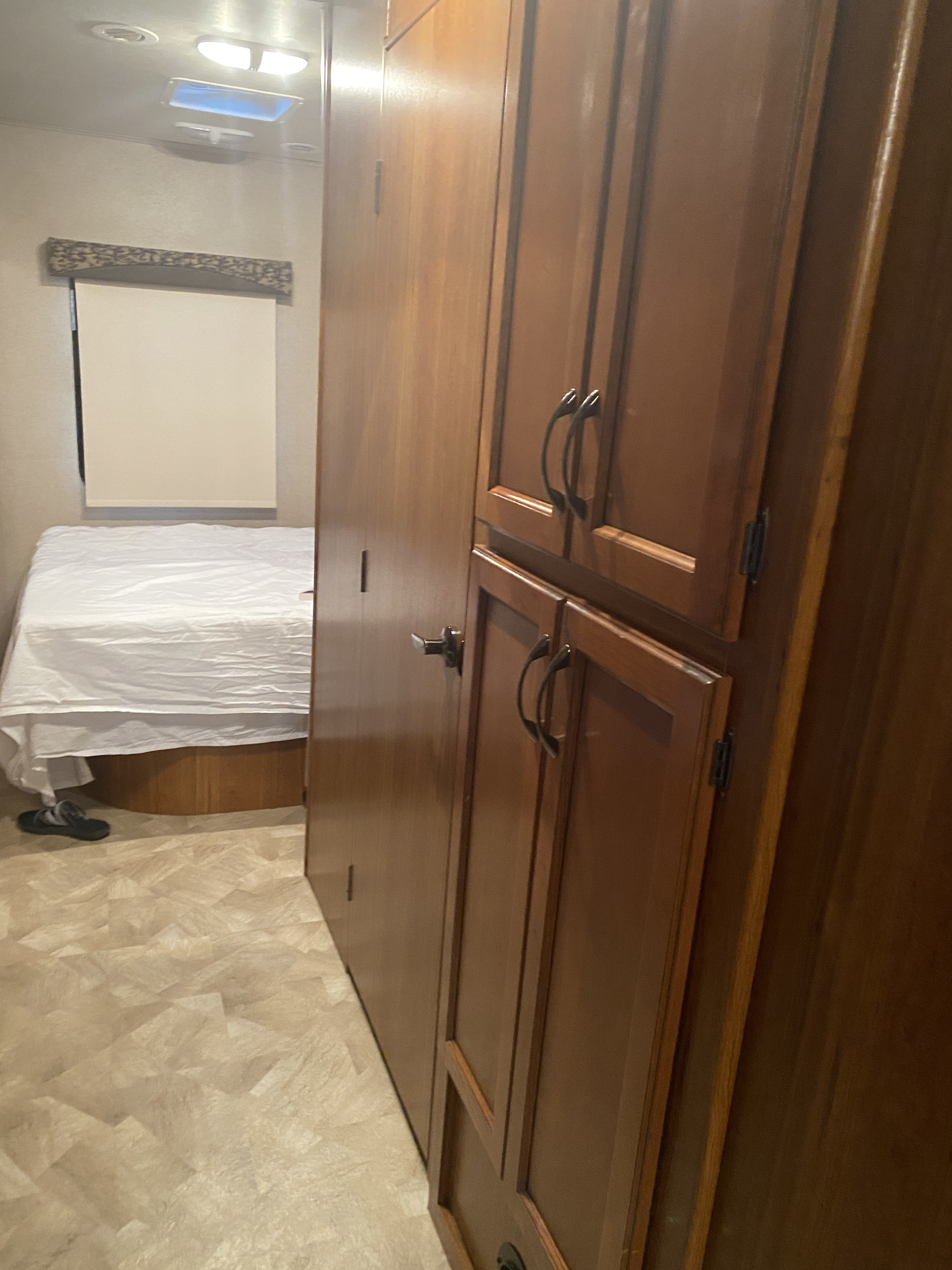 Neatly kept interior of an RV rental featuring a cozy bed with white sheets, warm wooden cabinets, and light patterned flooring.. Jayco Redhawk 2016