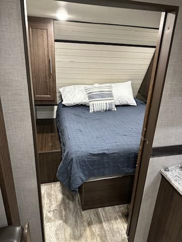RV rental bedroom interior: a compact space with a bed, blue comforter, white pillows, shiplap wall, and dark wood cabinetry.. Forest River Zinger Lite 280BH 2019