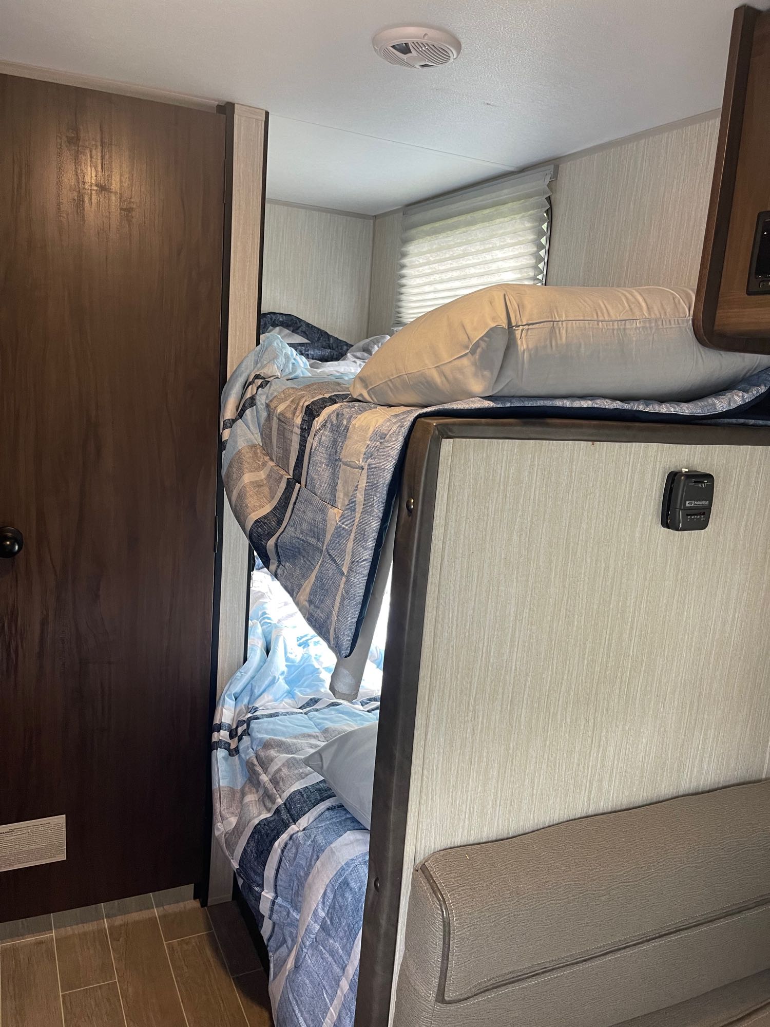 Cozy RV rental bunk beds with striped bedding inside a compact space, next to a door and a small thermostat.. Cherokee Wolf pup 2020
