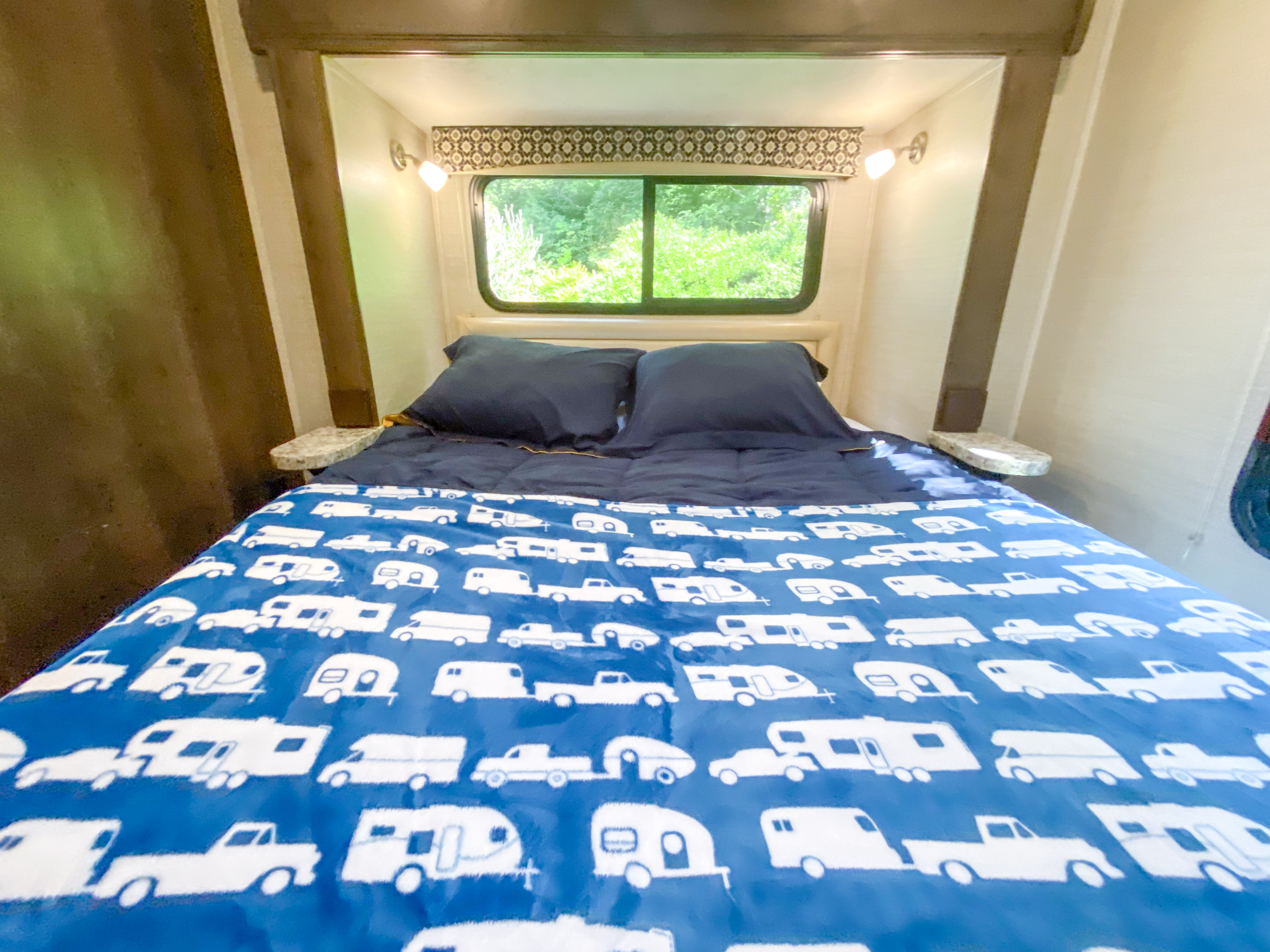 Inside a cozy **rv rental** bedroom. Features a bed with fun truck & trailer patterns, and a large window view.. Jayco Redhawk 2018