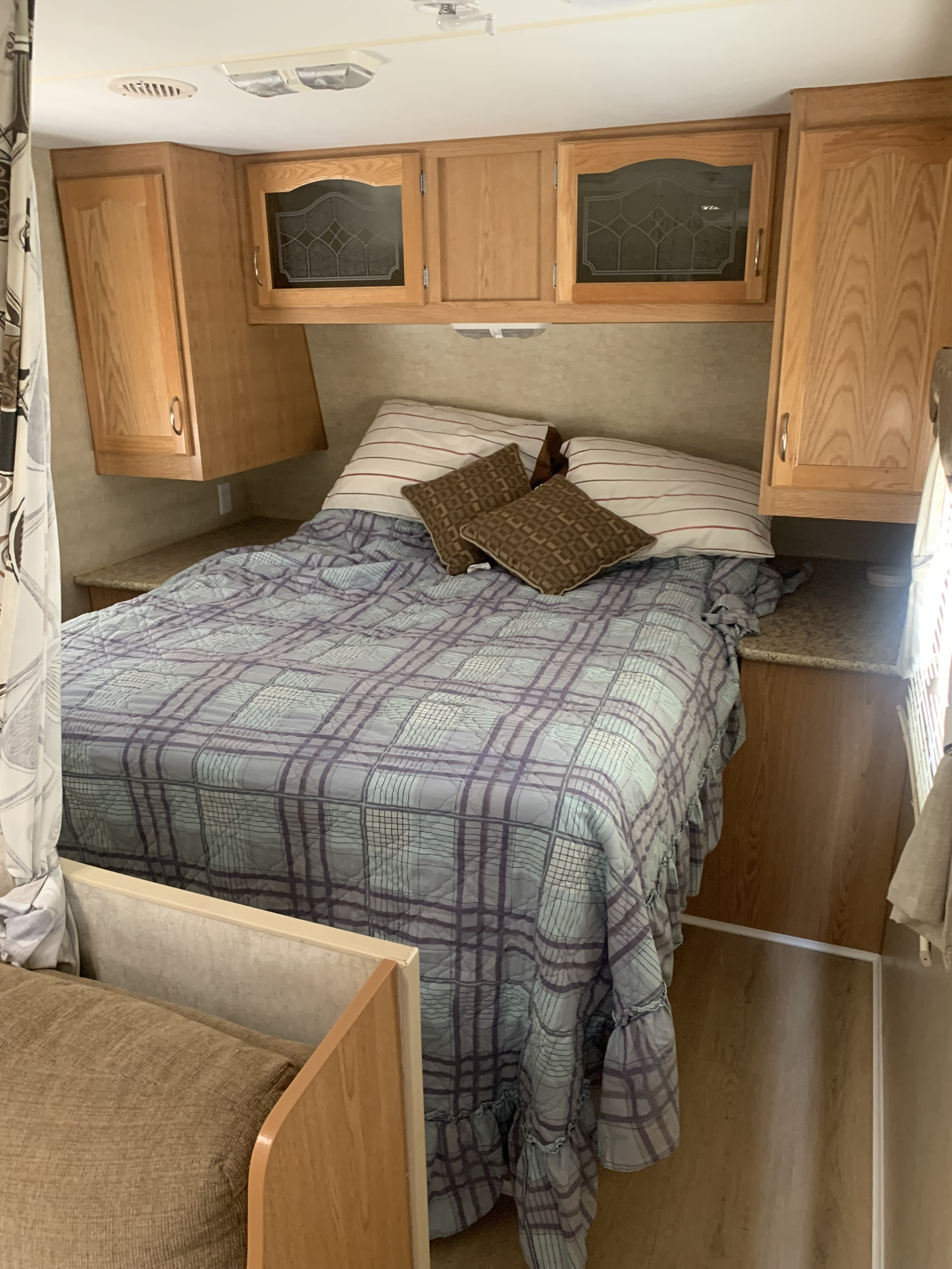 Cozy RV rental bedroom with a plaid bed, wood cabinets, and built-in storage, ideal for travelers.. Fleetwood Mallard 2008