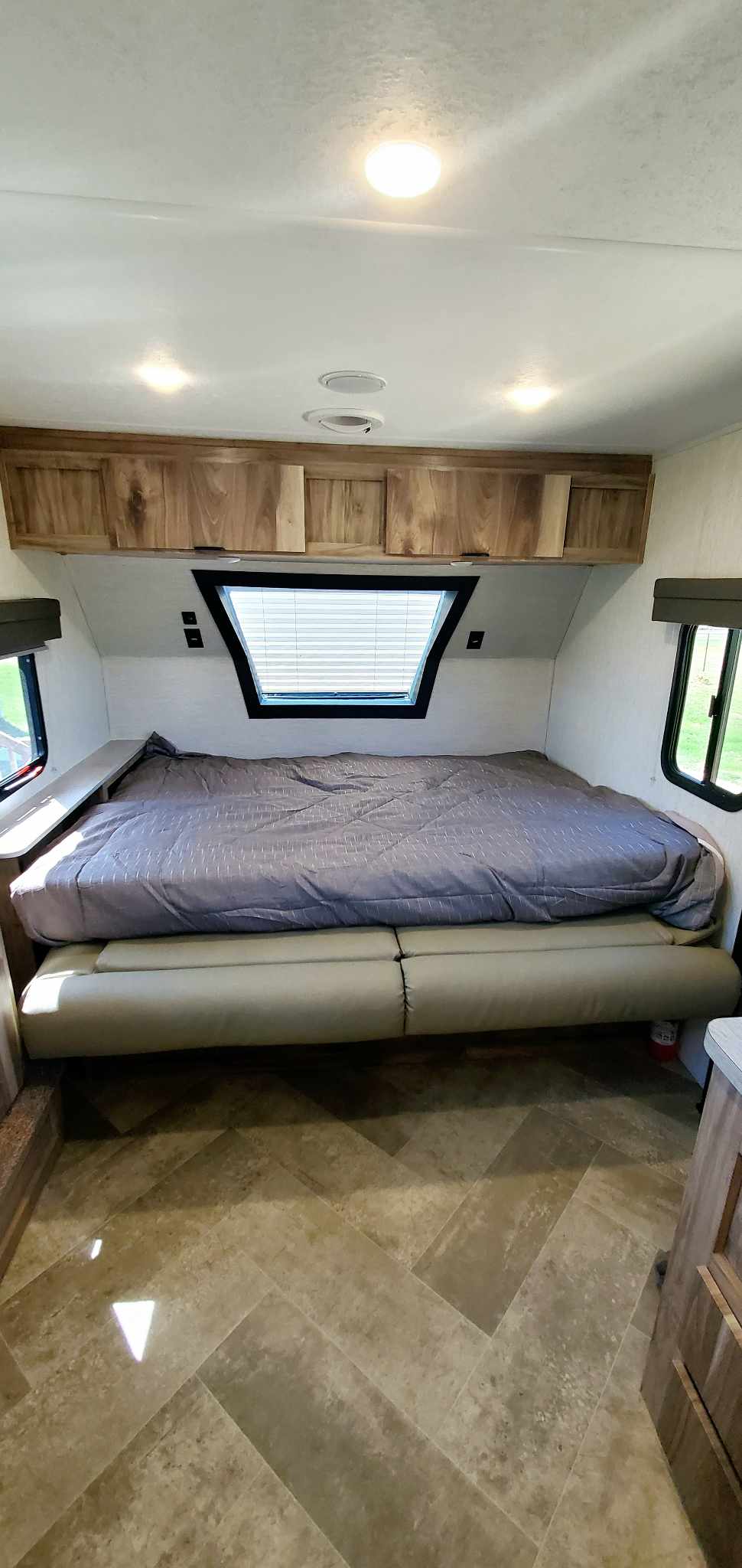 This RV rental bedroom features a cozy bed, overhead cabinets, and a unique trapezoidal window.. Palomino 189BHS 2022