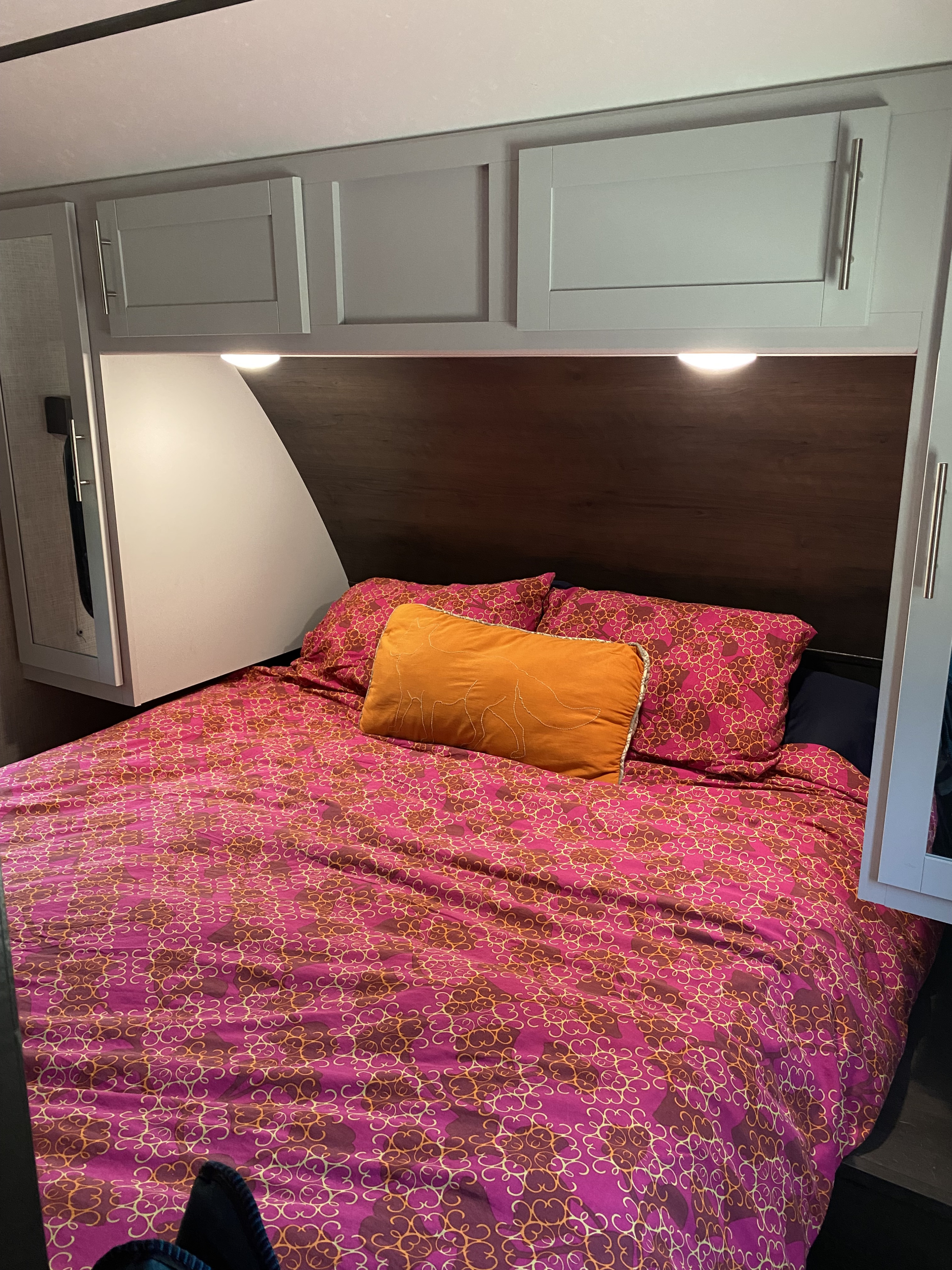 Cozy RV rental bedroom with a vibrant patterned bed, overhead cabinets, and soft lighting for a comfortable stay.. Keystone RV Bullet Ultra Lite 2019