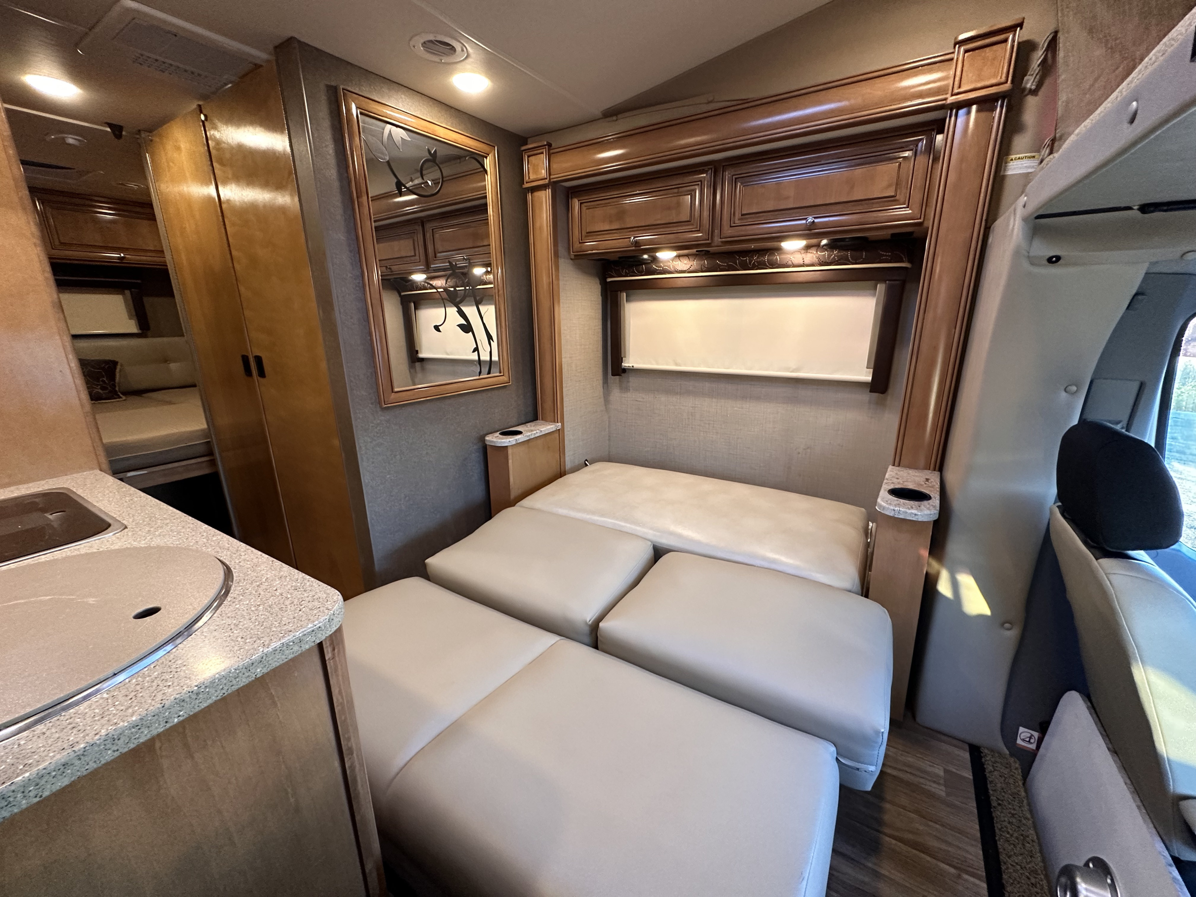 Explore this rv rental's compact interior, featuring a convertible bed, small kitchen counter, and elegant wood cabinetry.. Thor Synergy 2016