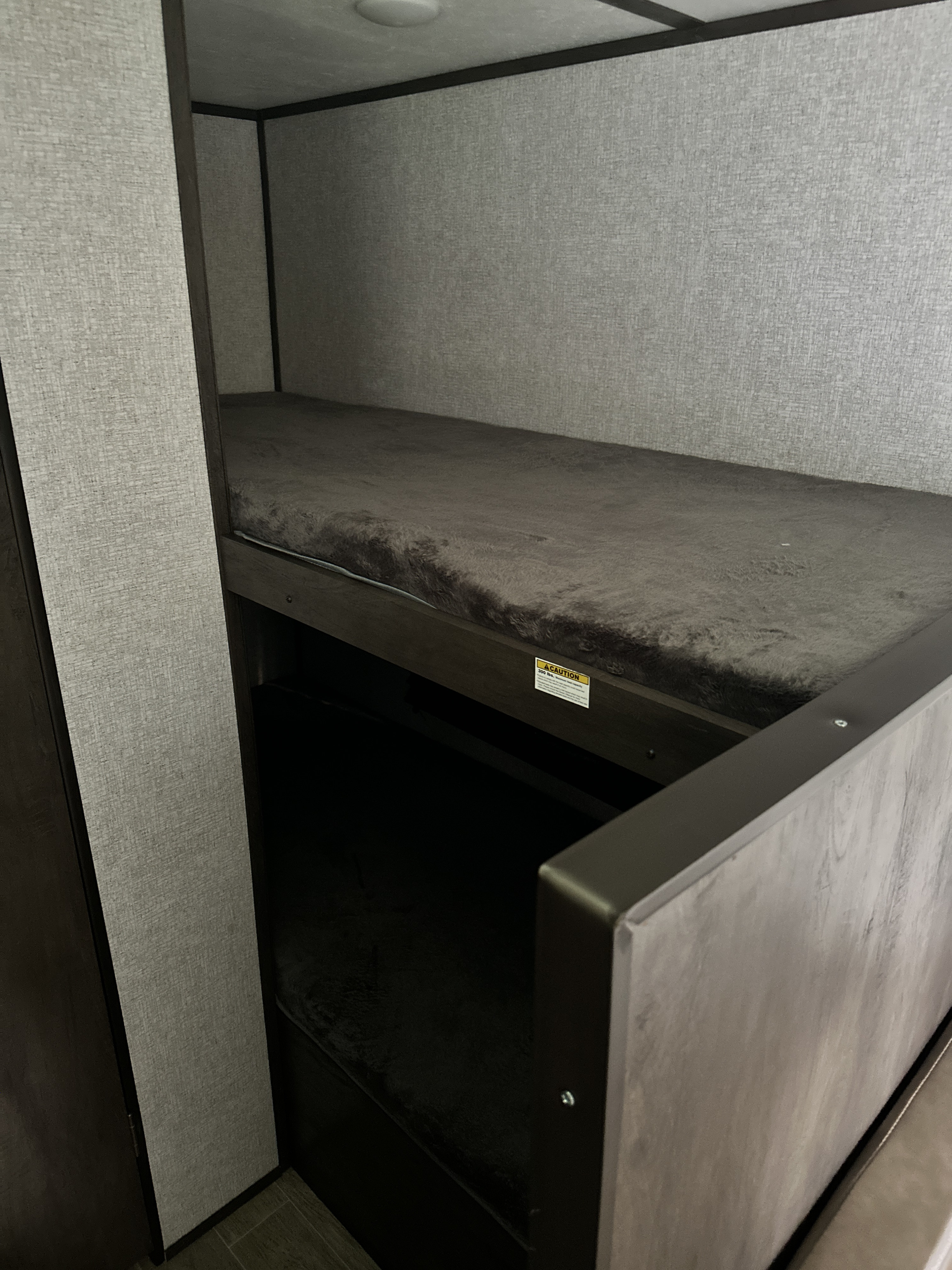 Inside an RV rental, a set of cozy bunk beds with dark grey fluffy mattresses and textured grey walls.. Dutchmen Coleman Lantern LT 2020