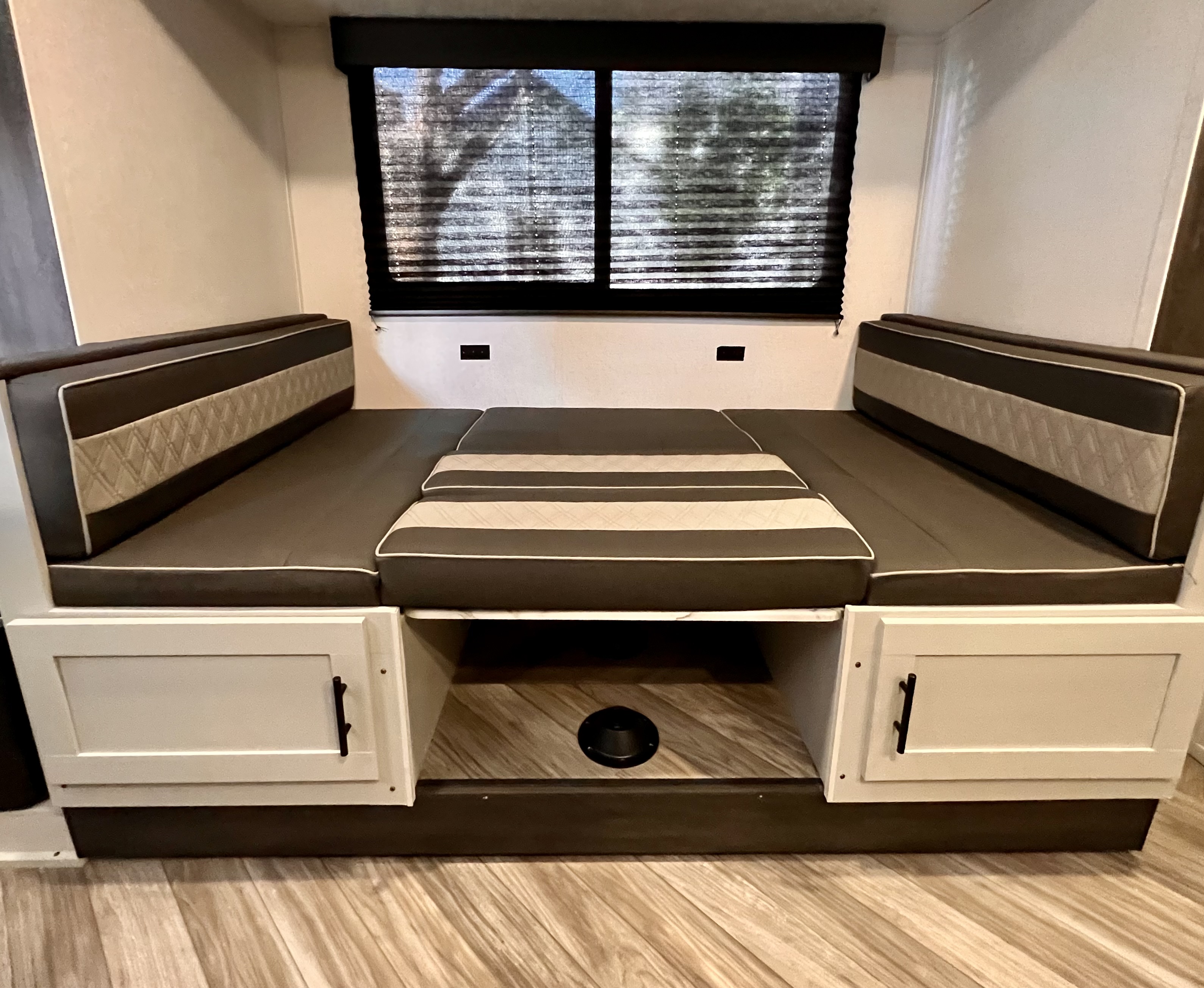 RV rental dinette area with dark gray and light gray patterned cushions, converting to a bed. Window with blinds, storage cabinets below.. Forest River Wildwood FSX 2022