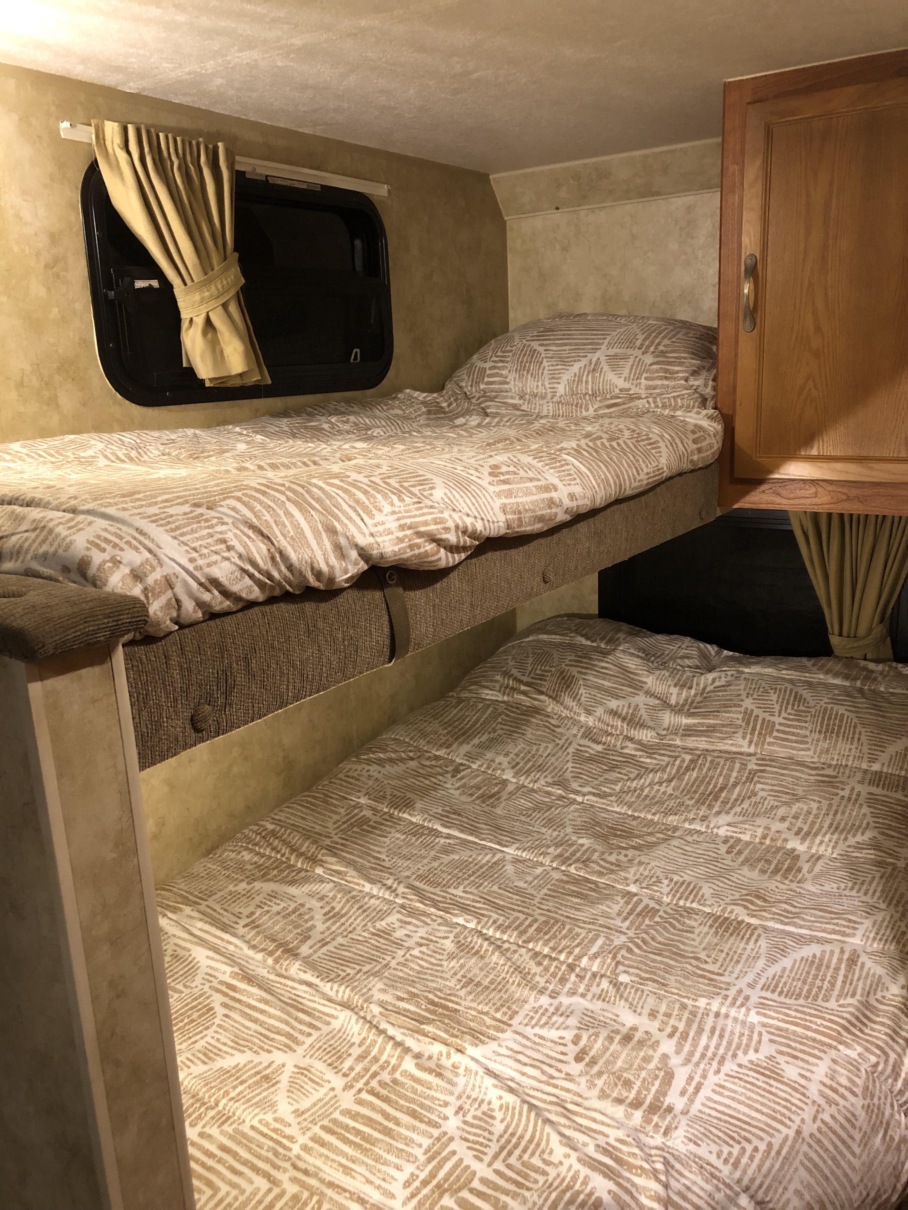 Cozy RV rental interior featuring two comfortable bunk beds with patterned bedding, a window, and a wooden cabinet.. Starcraft Travel Star Sport 2010