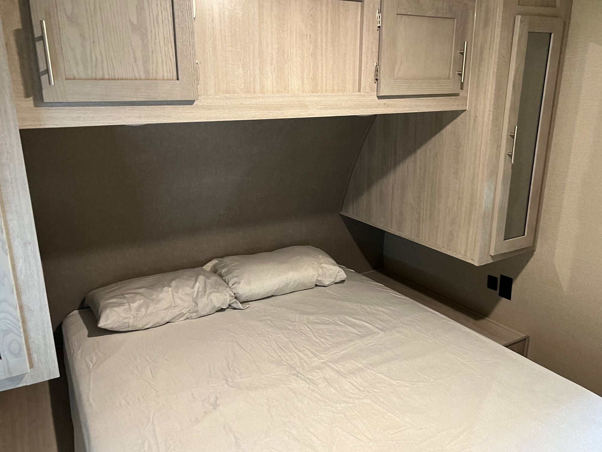 Inside this RV rental, a compact bedroom features a bed with light sheets and pillows, plus light wood-grain overhead cabinets.. Forest River Coachmen Catalina Legacy 2022