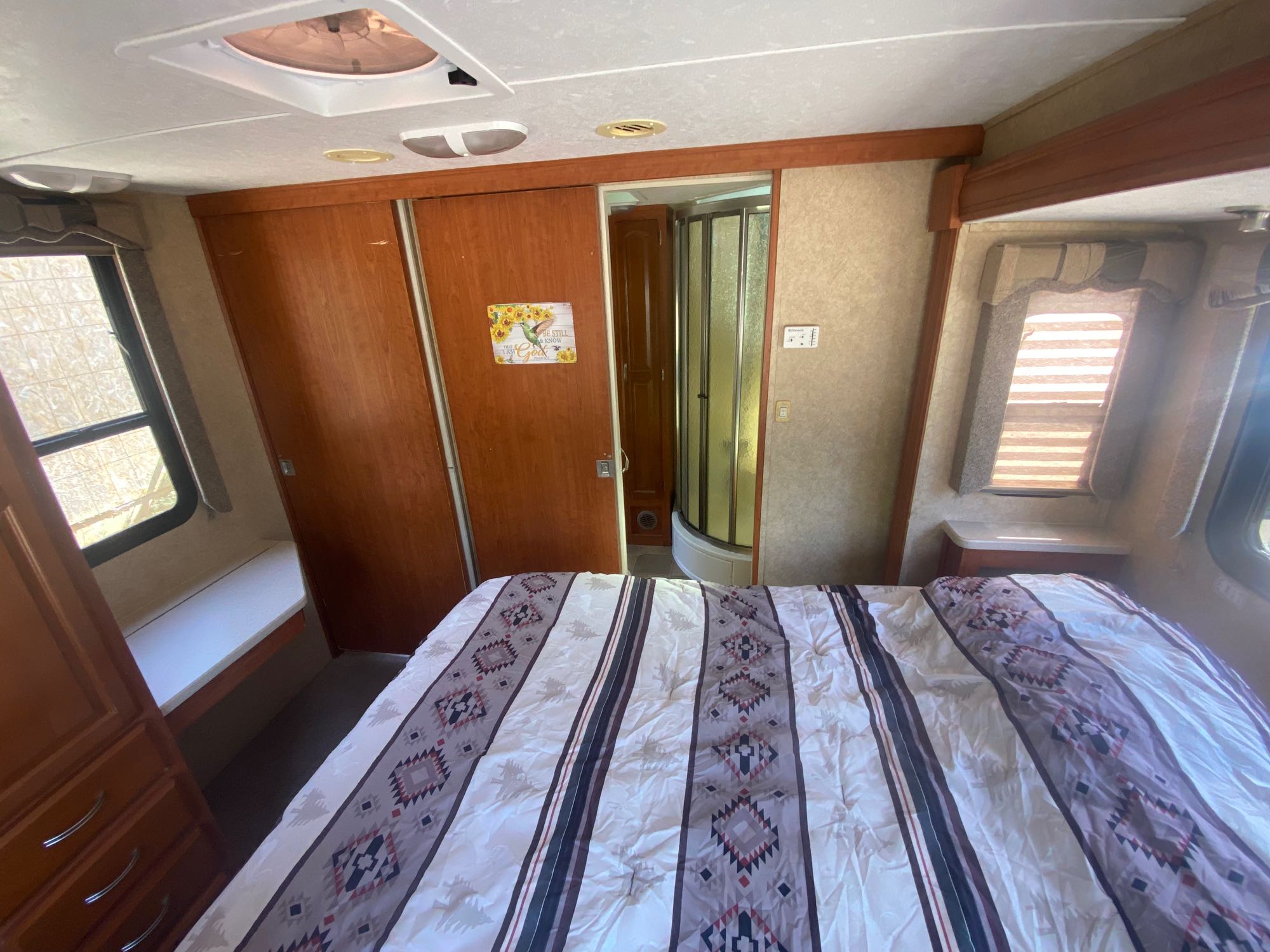 Spacious RV rental bedroom with patterned bed, full shower, and wooden storage. Ideal for your next journey.. Forest River Sunseeker 2010