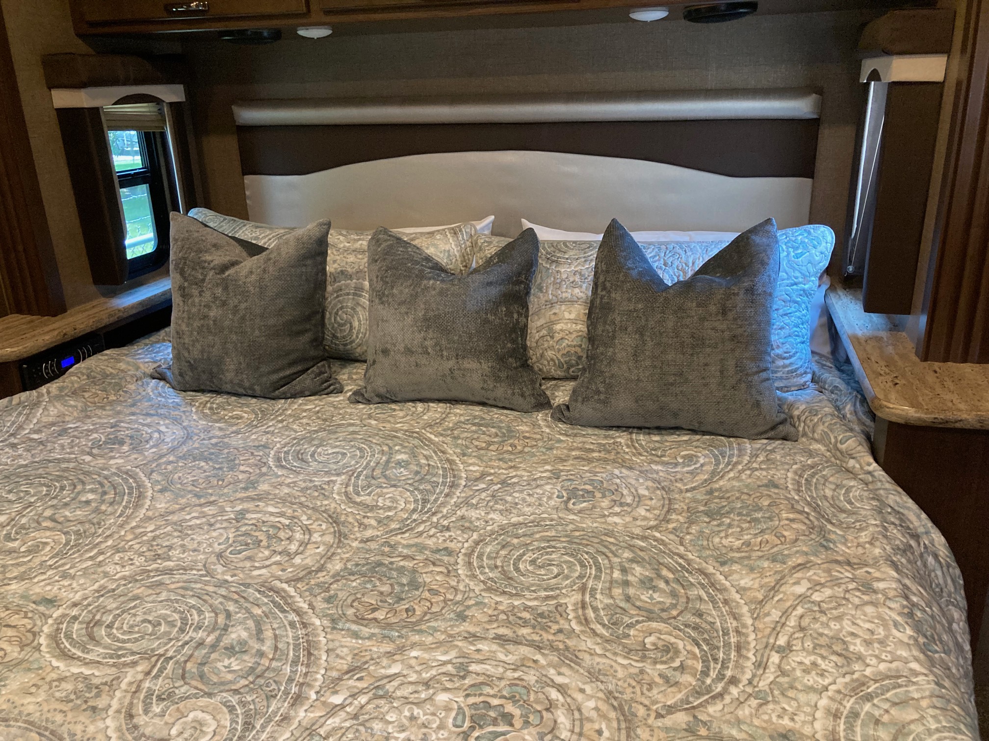 This RV rental bedroom features a comfy bed with a paisley comforter, gray pillows, and a padded headboard.. Thor A.C.E. 2017