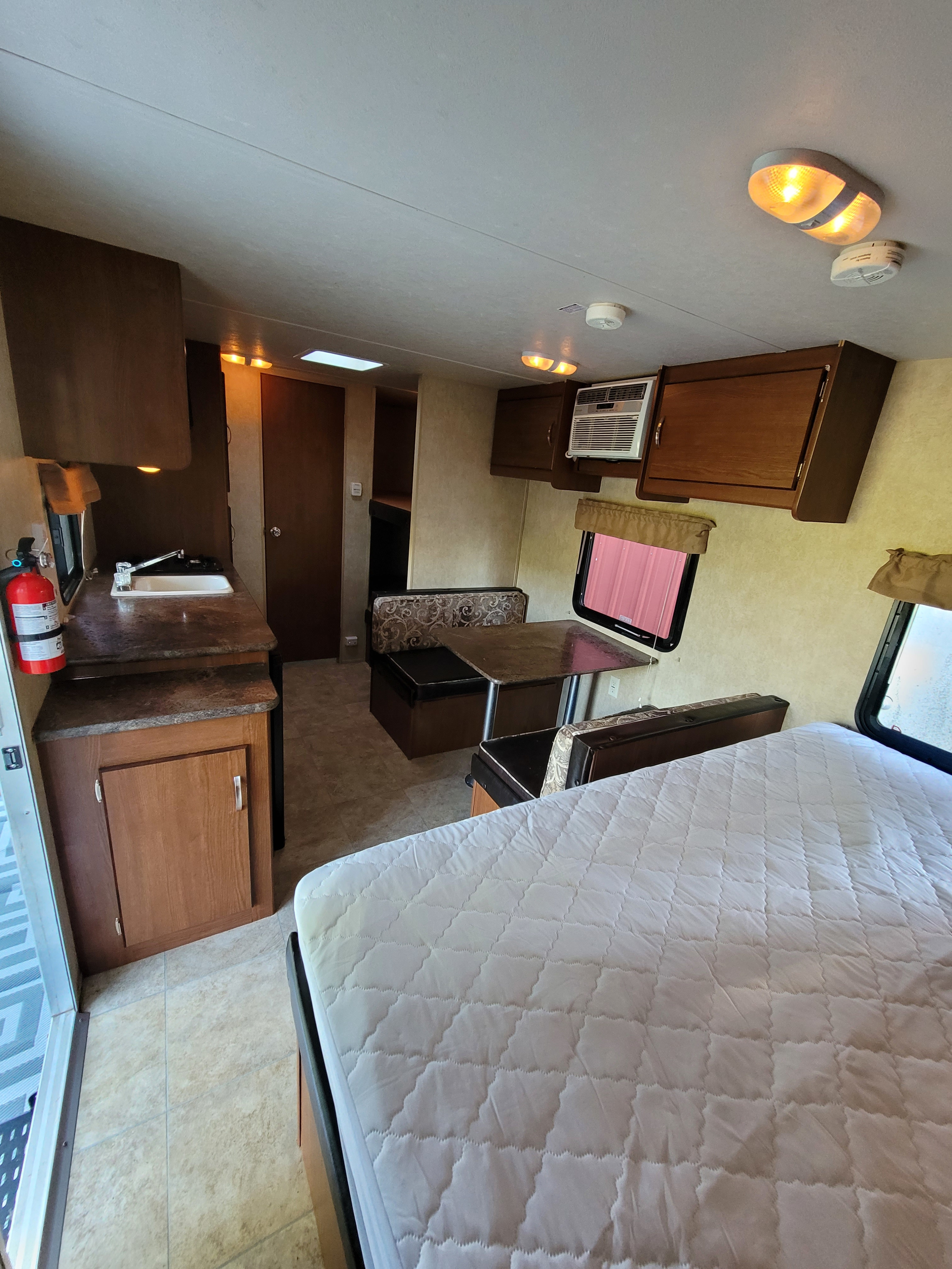 Bright RV rental interior with a kitchenette, dinette, bed, and overhead storage. Ideal for travel.. Forest River Wildwood X-Lite 2014