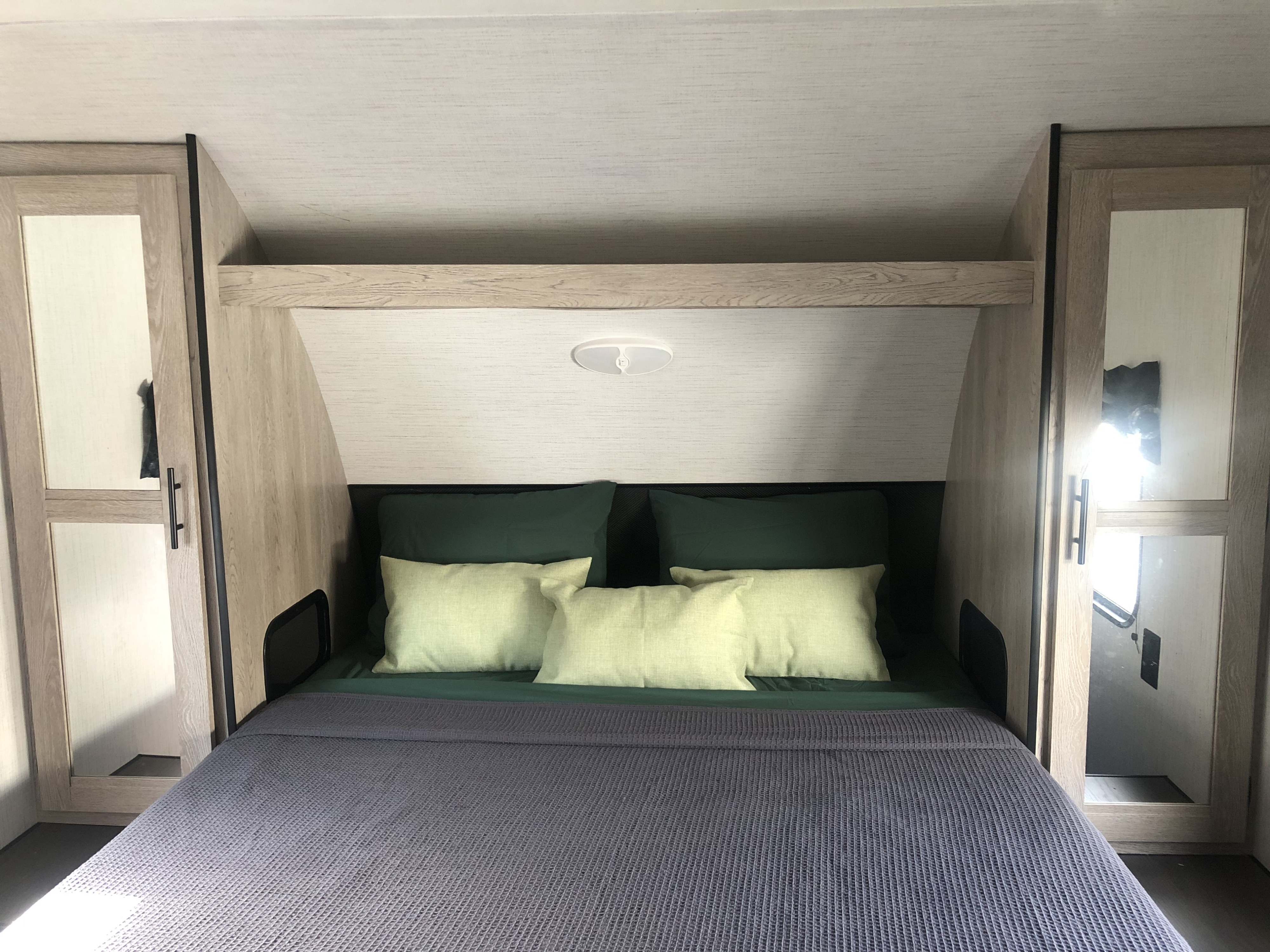 Cozy RV rental bedroom featuring a neatly made bed with dark green and light green pillows, flanked by light wood cabinets.. Heartland RVs Prowler 2022