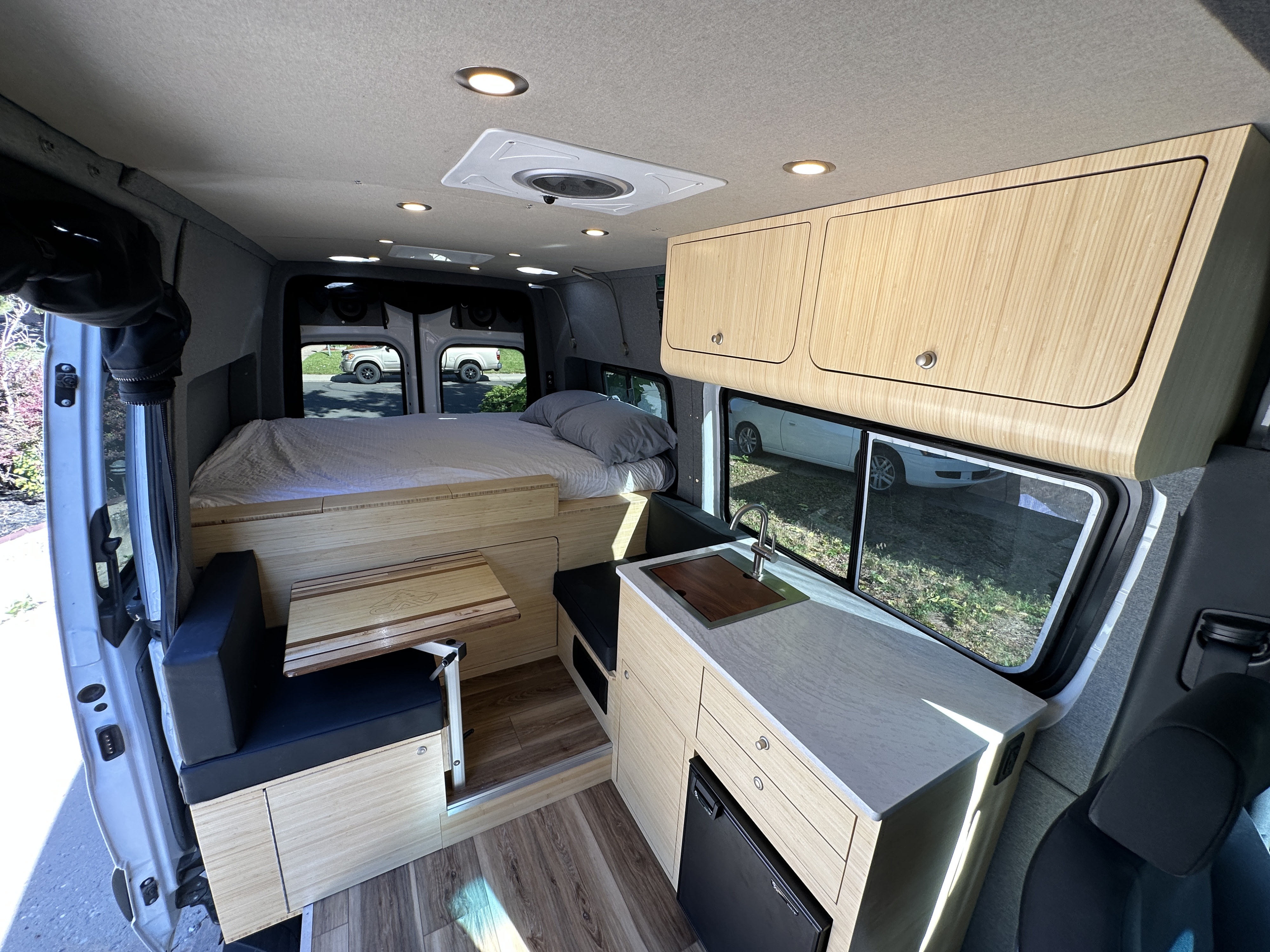 Bright RV rental interior: Light wood cabinetry, sink, mini-fridge, bed, and dinette make for a functional camper van.. Mercedes-Benz Sprinter 2019