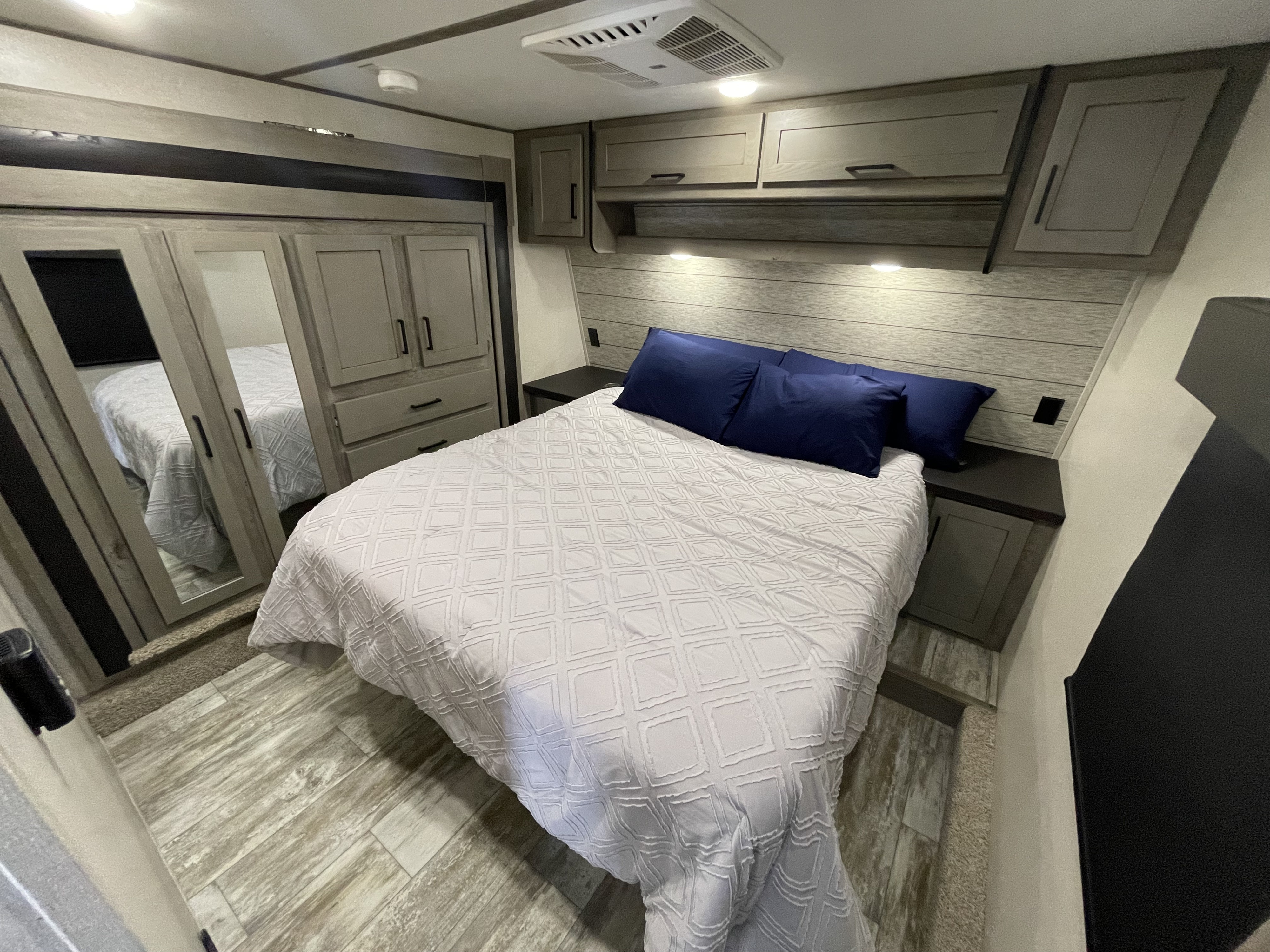 Modern RV rental bedroom with a large bed, navy pillows, overhead cabinets, and a mirrored wardrobe for comfortable stays.. Keystone Carbon 2021